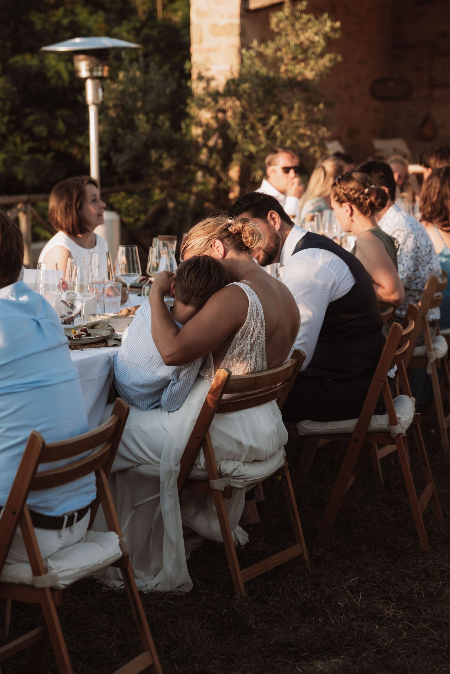 Wedding guests seated at an outdoor reception dinner table with patio heater and wine glasses at sunset.