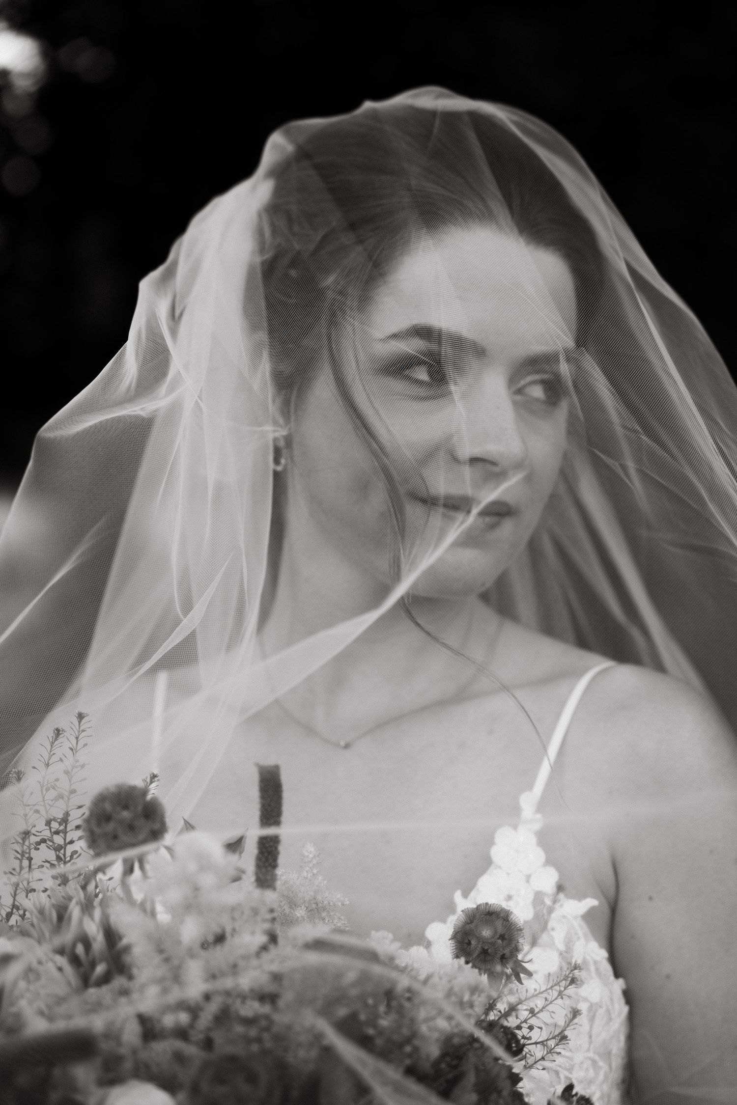 Dramatic black and white bridal portrait with flowing veil creating ethereal effect.