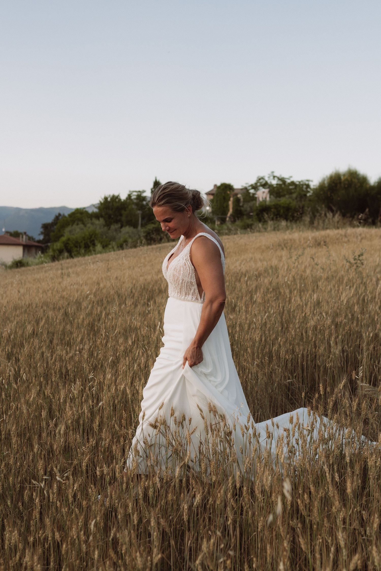 A person in a white wedding dress sits thoughtfully in a golden wheat field at sunset.