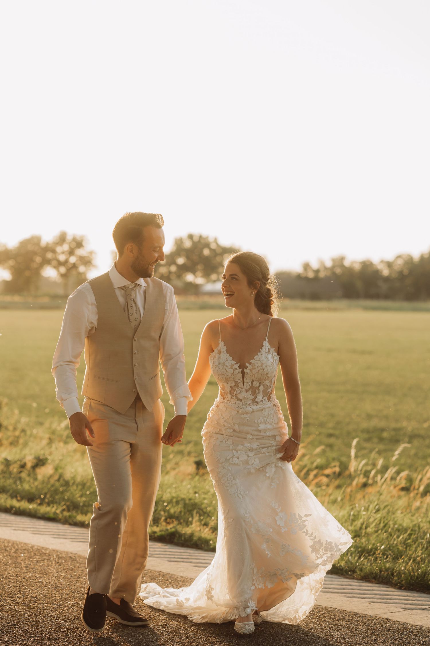 Couple walking together at sunset in a grassy field wearing wedding attire.