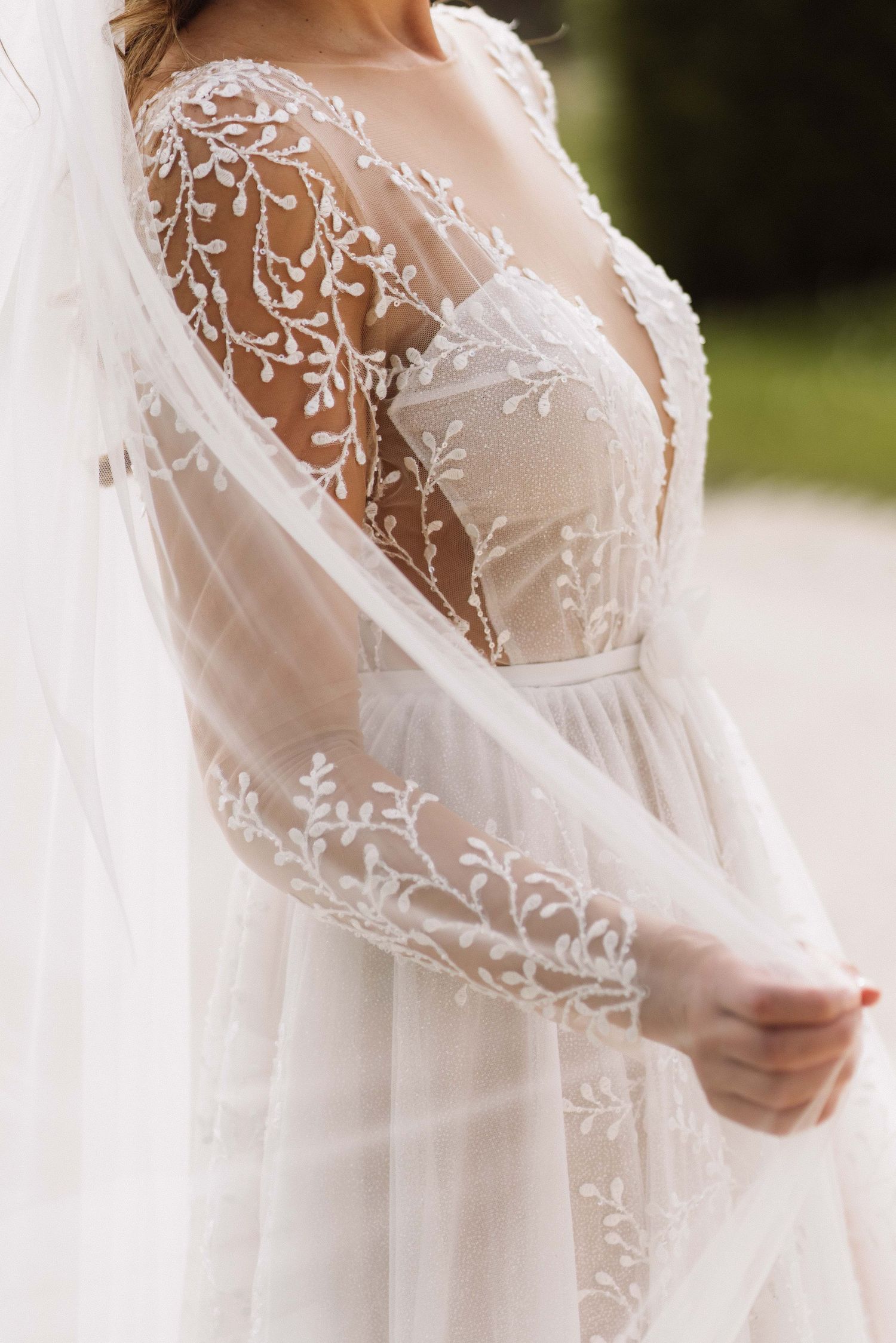 Close-up detail of delicate floral lace sleeves and bodice on a white wedding gown with flowing tulle veil.