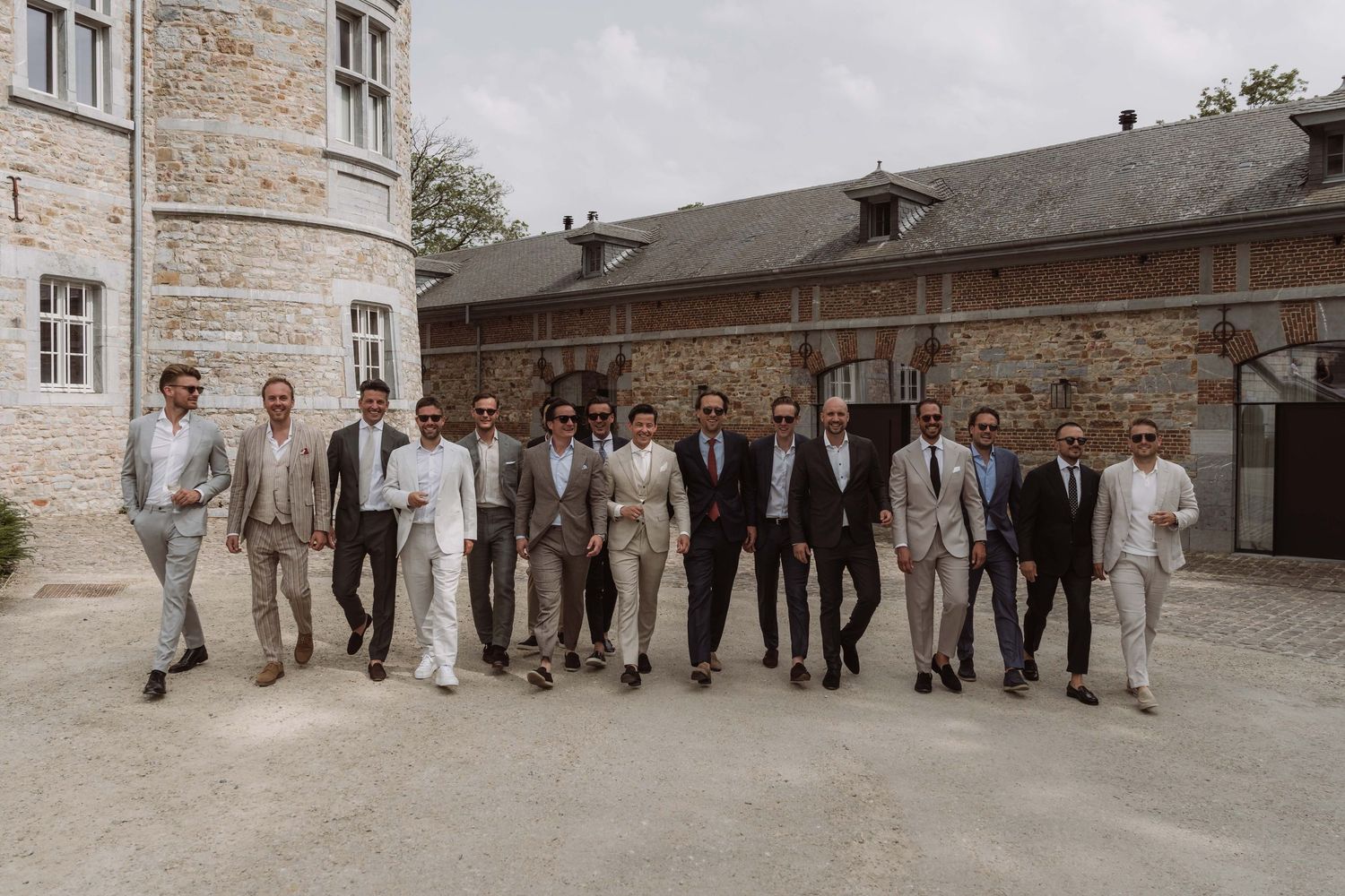 A wedding party in gray suits poses together in front of a stone building exterior.