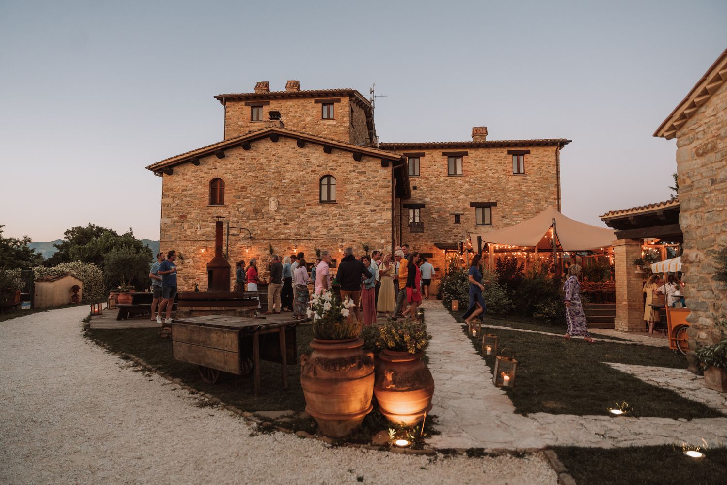 Rustic Italian villa with stone walls and terracotta pots along a gravel path at sunset in Tuscany.