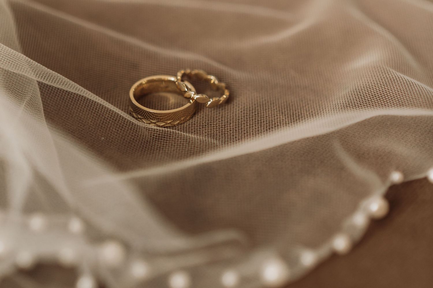 Two gold wedding rings rest on a soft white tulle fabric with delicate folds creating an elegant bridal detail.