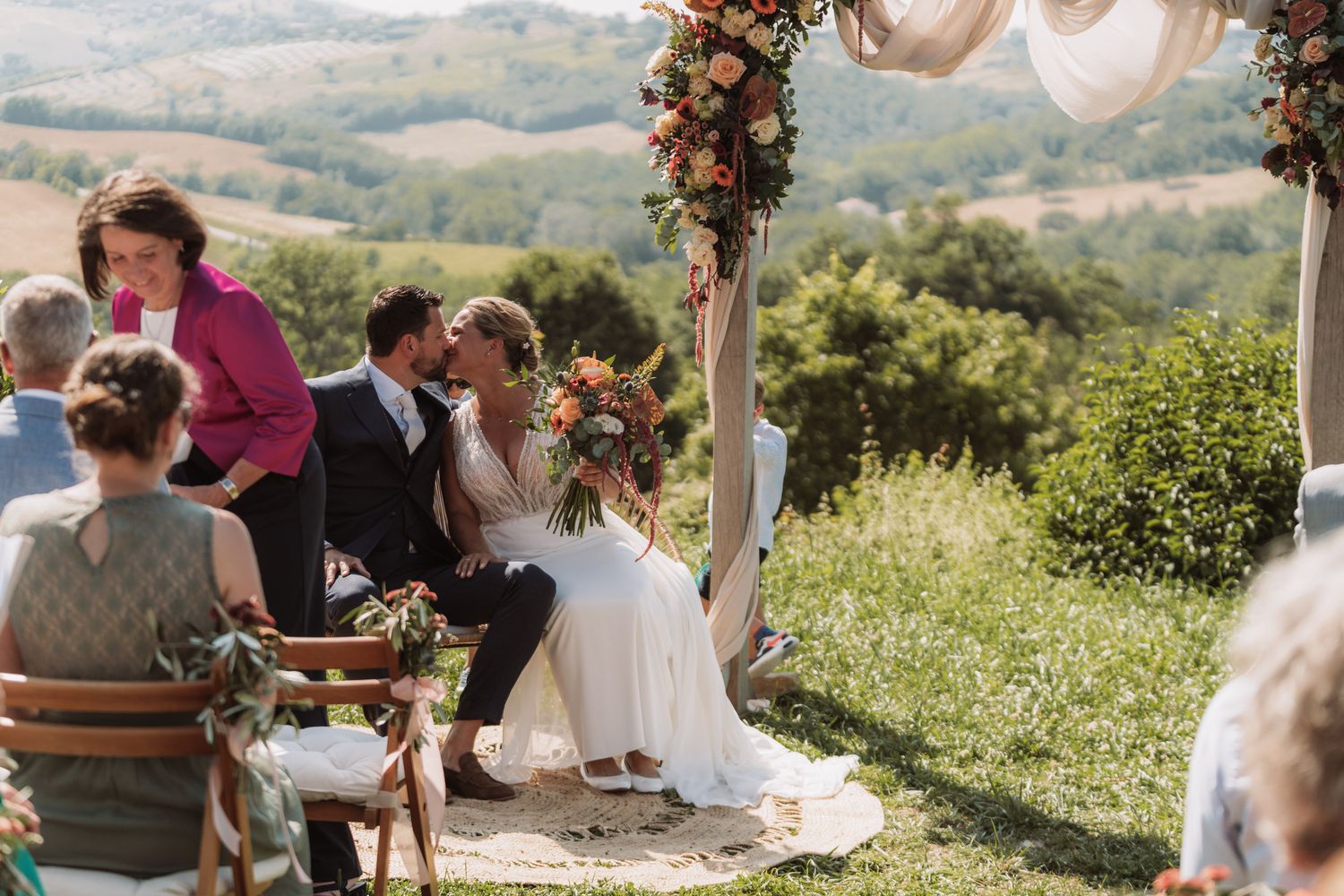 Outdoor wedding ceremony in a rustic setting with floral arch overlooking scenic mountain landscape.