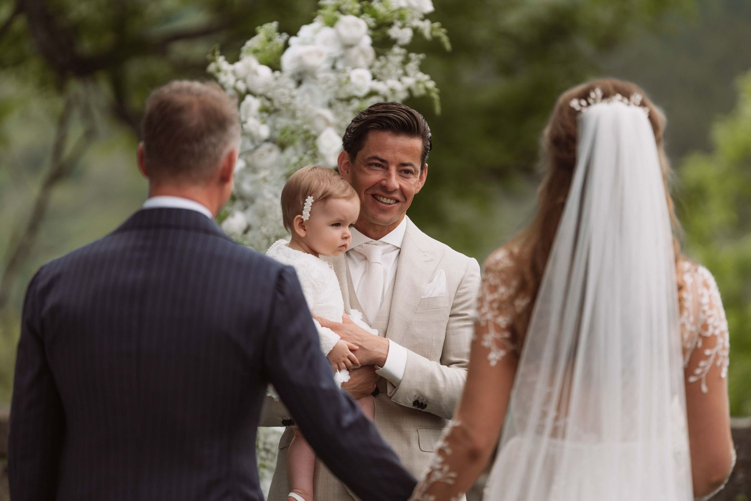 A wedding ceremony takes place outdoors with white floral arrangements and guests gathered to celebrate the special occasion.
