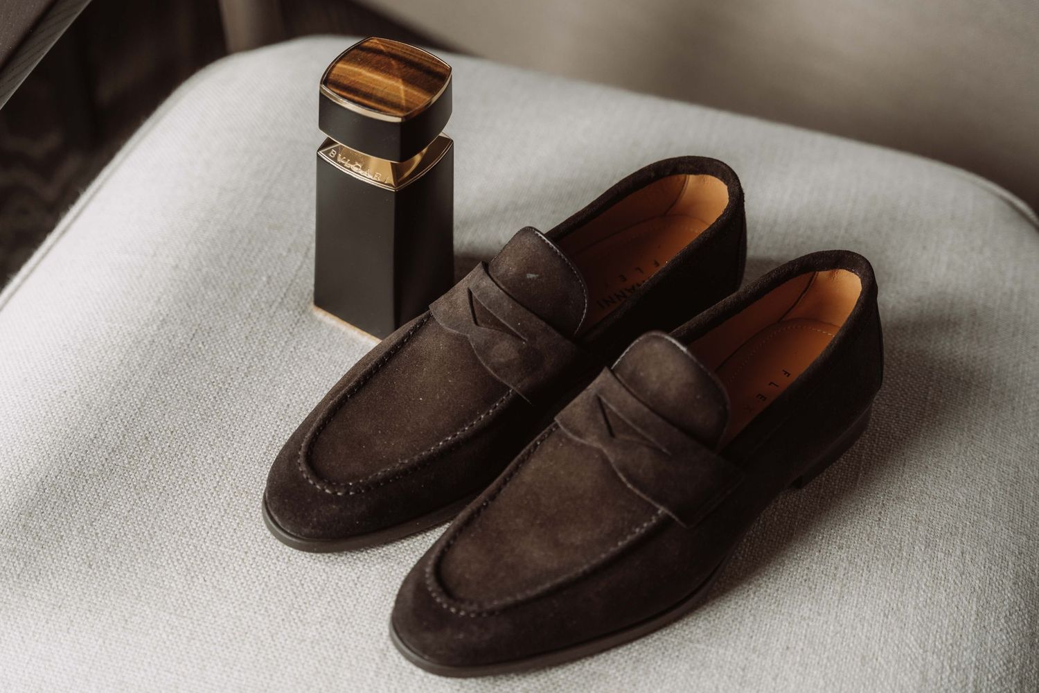 A dark brown suede penny loafer shoe shown from multiple angles on a white surface.
