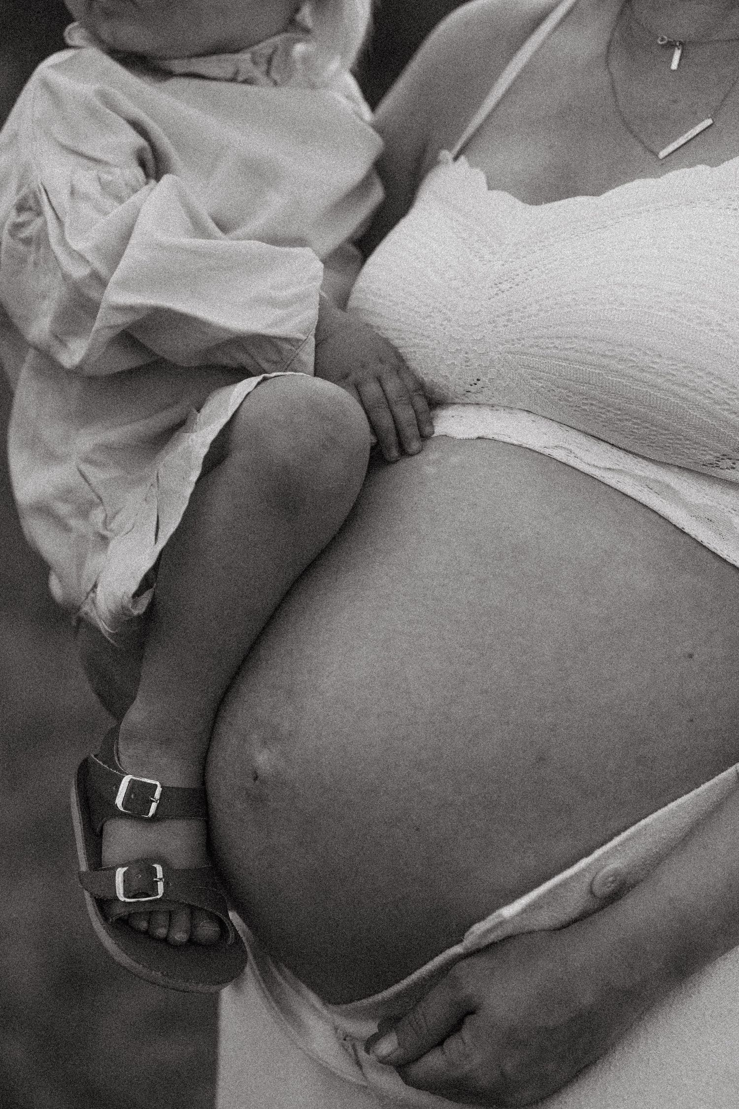 Black and white close-up of a pregnant belly with hands gently resting on top.