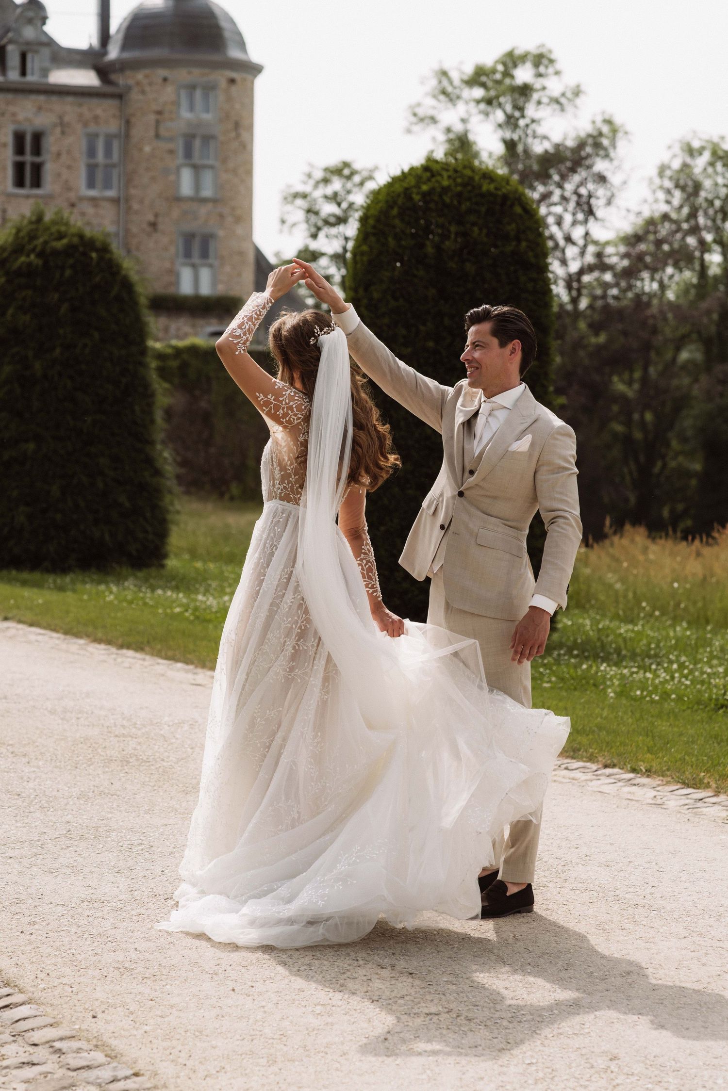 A couple in wedding attire dances gracefully on a stone path outside a historic chateau in France.