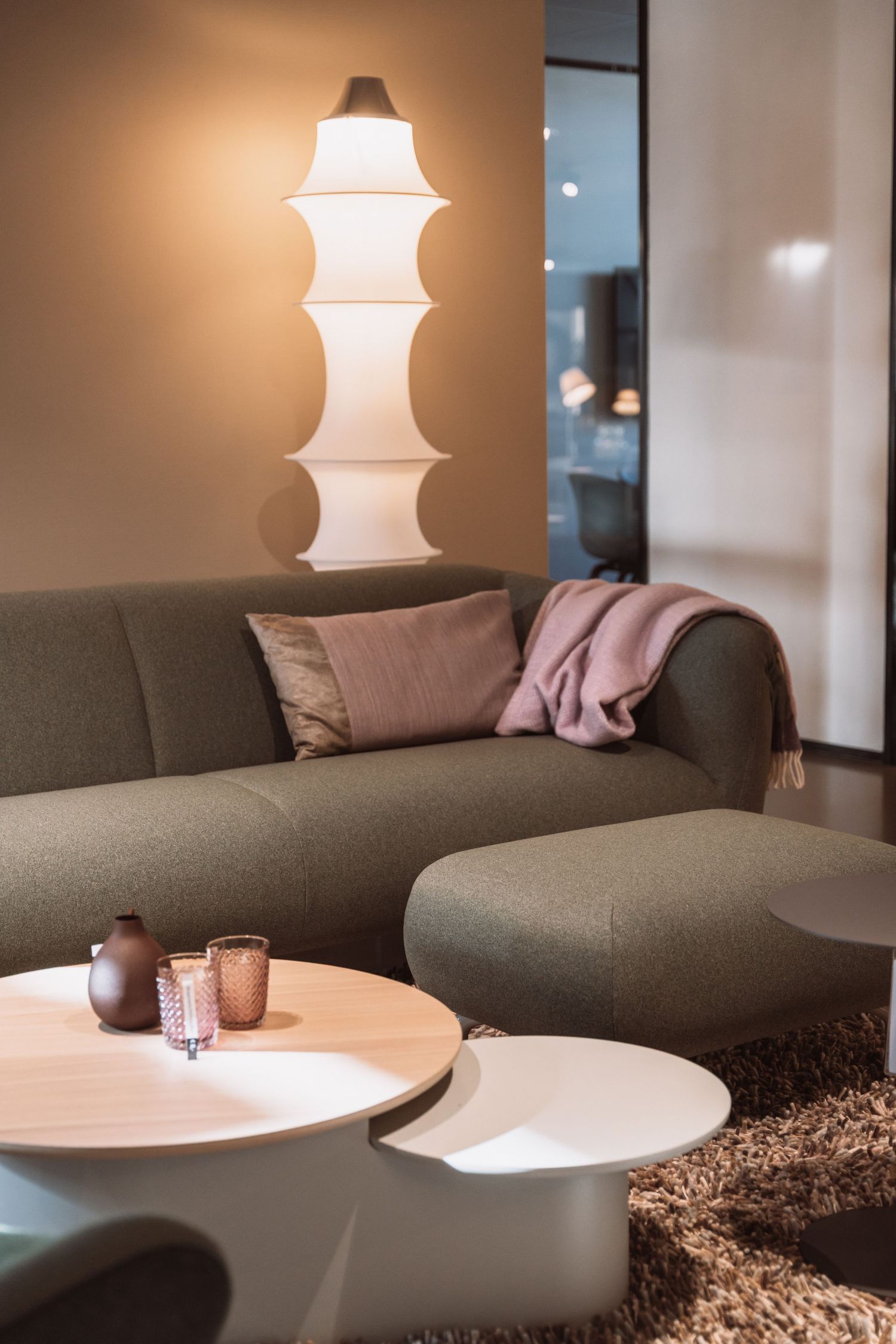 Modern living room interior with curved white coffee tables, gray sofa and elegant pendant lamp creating ambient lighting.