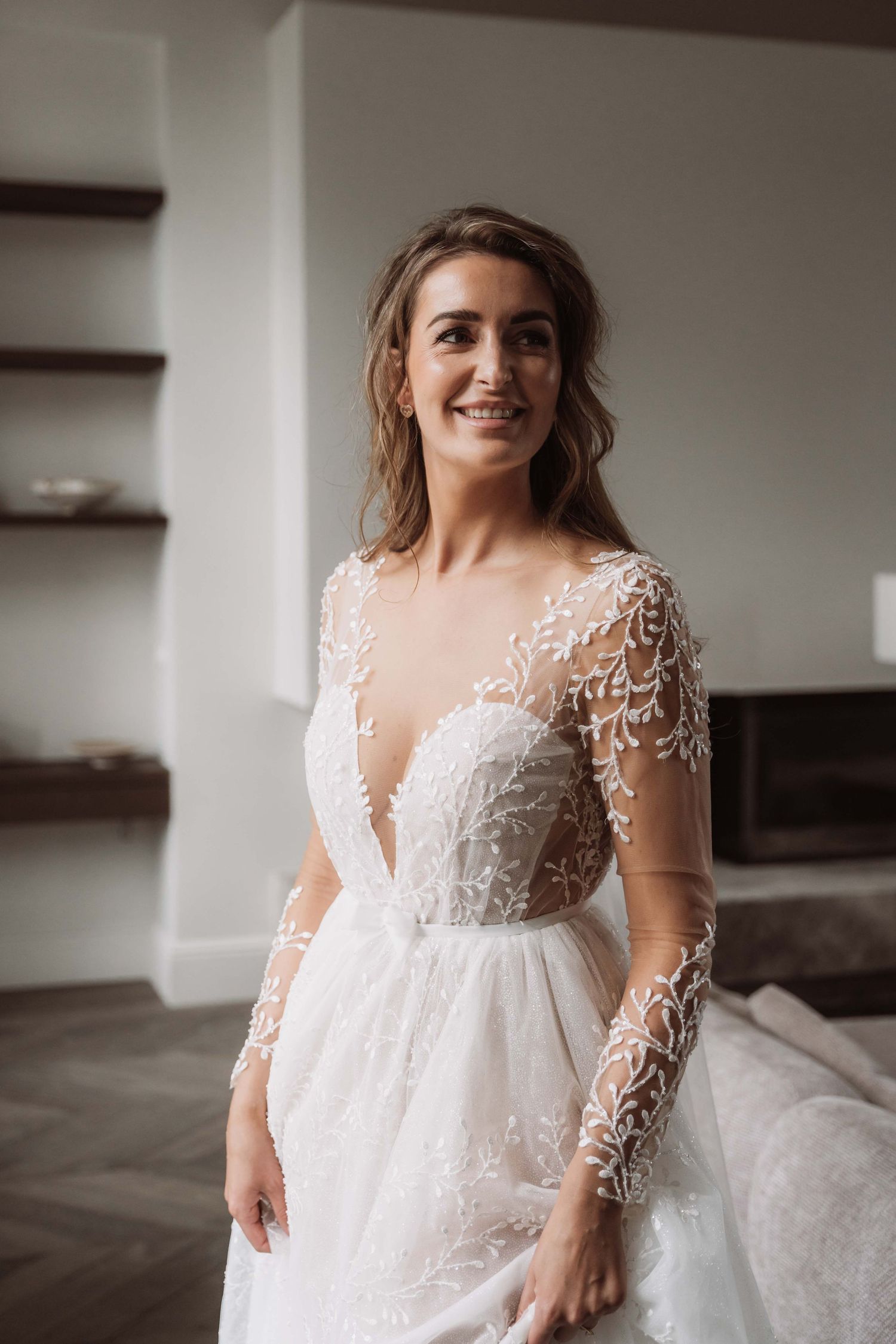 Elegant white lace wedding dress with long sheer sleeves and empire waist shown in romantic bridal portrait series.