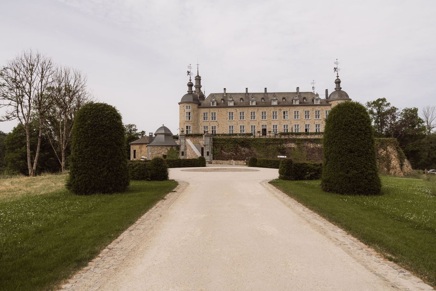 A long driveway leads up to a grand historic mansion through manicured grounds and topiary gardens.