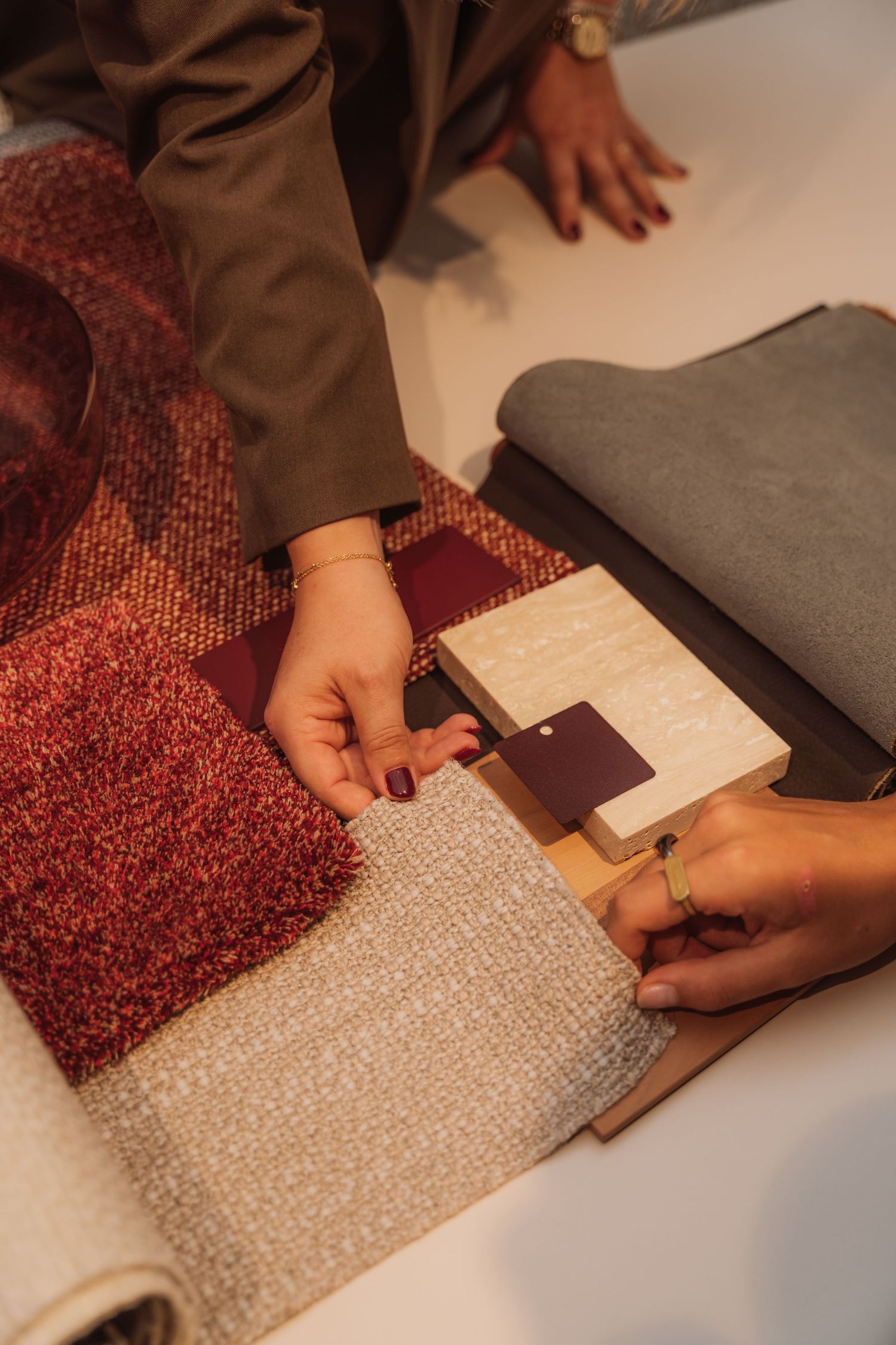 Hands examining fabric swatches and material samples on a surface.