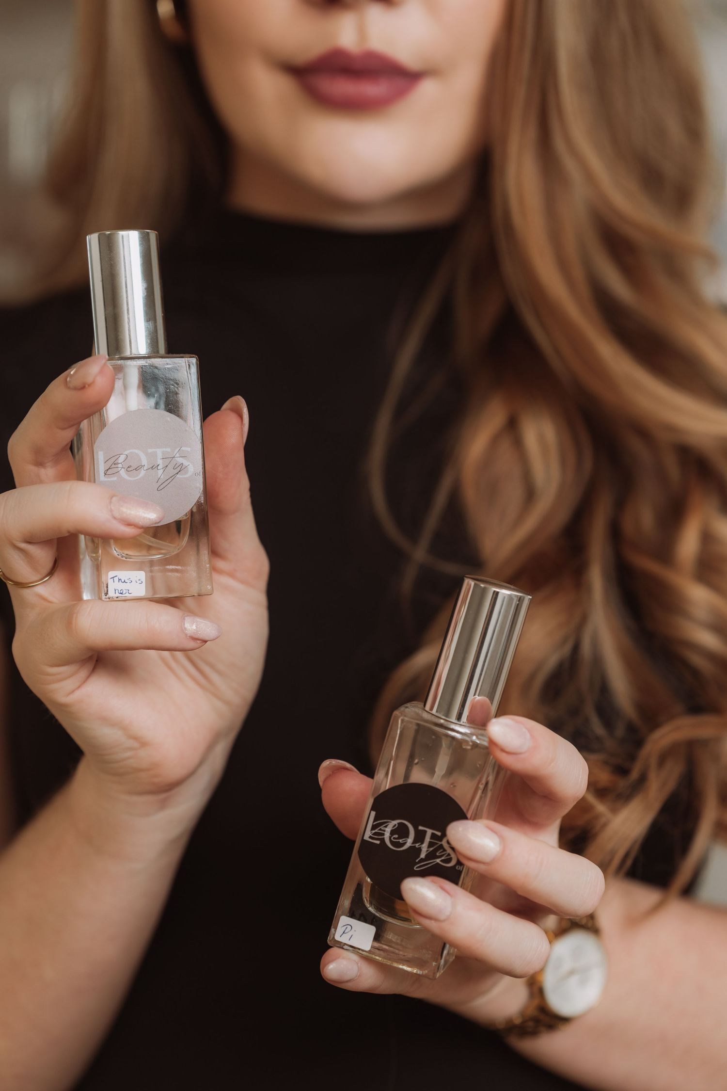 Hands holding clear glass perfume bottles against dark background.