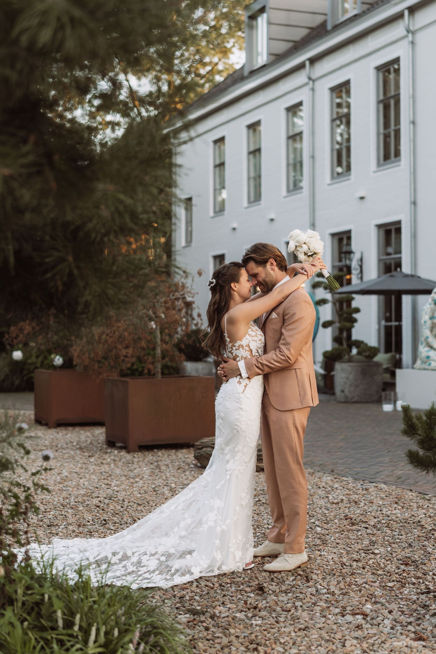 A romantic outdoor wedding moment captured at a white mansion with gravel paths and elegant landscaping details.