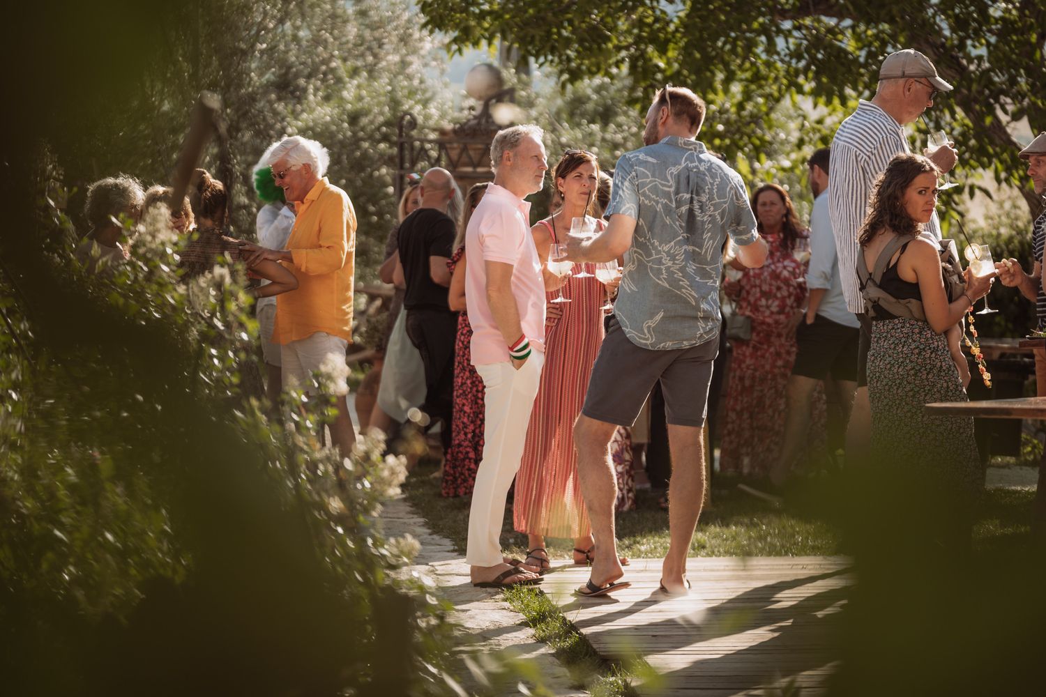 People gather in a sunlit garden setting for an outdoor social event on a summer afternoon.