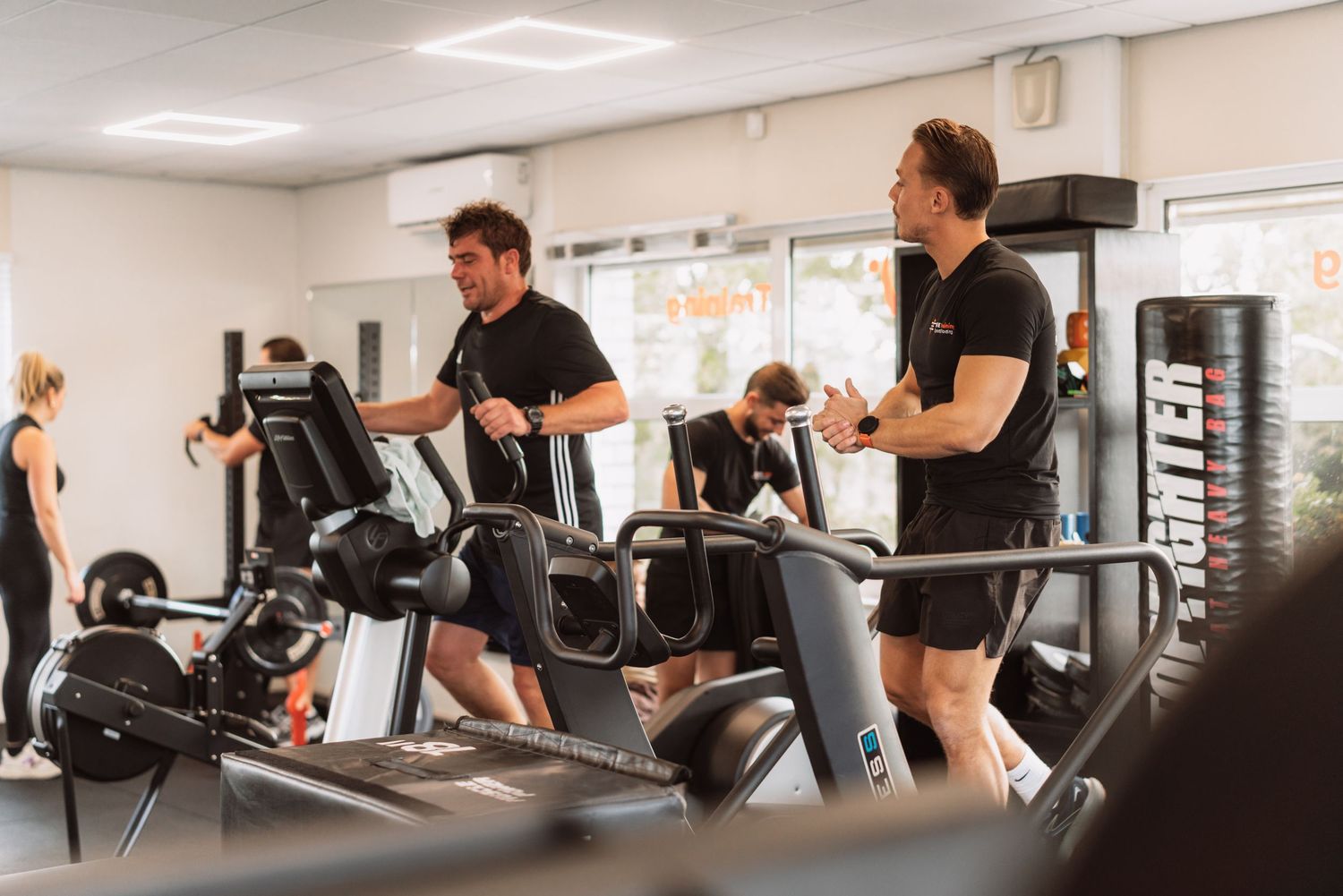 People working out on cardio equipment in a modern fitness facility with exercise machines and gym equipment.