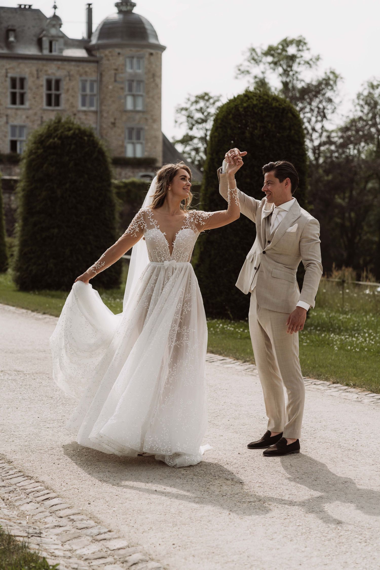 A couple shares a romantic moment dancing on a path outside a majestic French chateau on their wedding day.