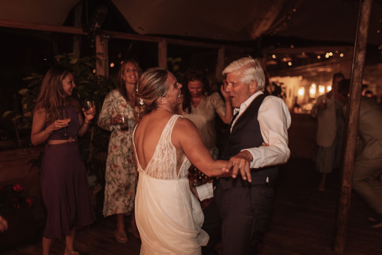 A group of people dancing and celebrating at a dimly lit evening wedding reception.