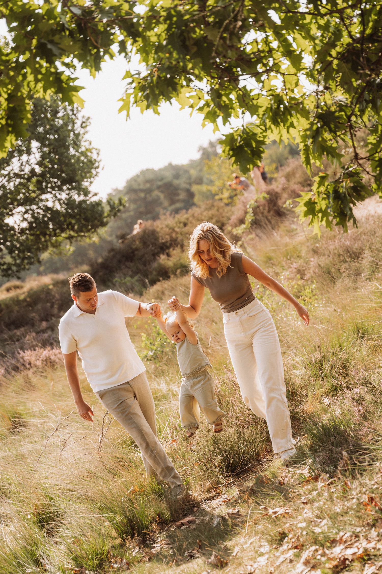 Family playing and walking together on a sunny hillside path.