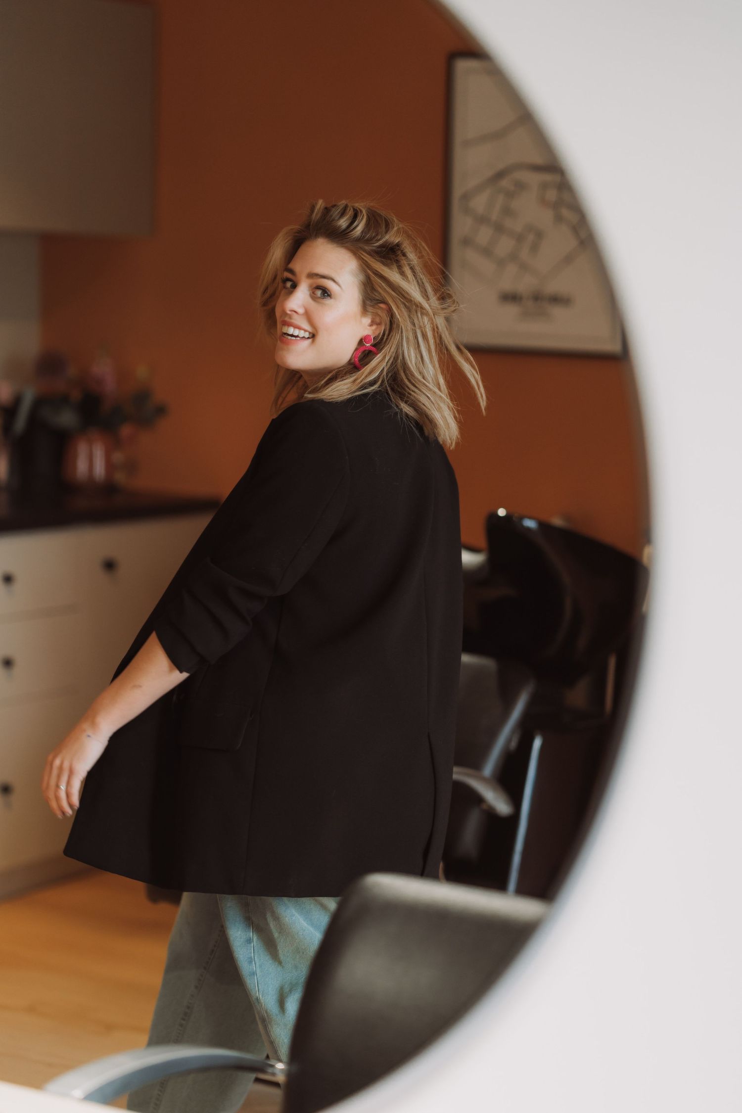 Person in black outfit sitting in a casual indoor setting with warm lighting.