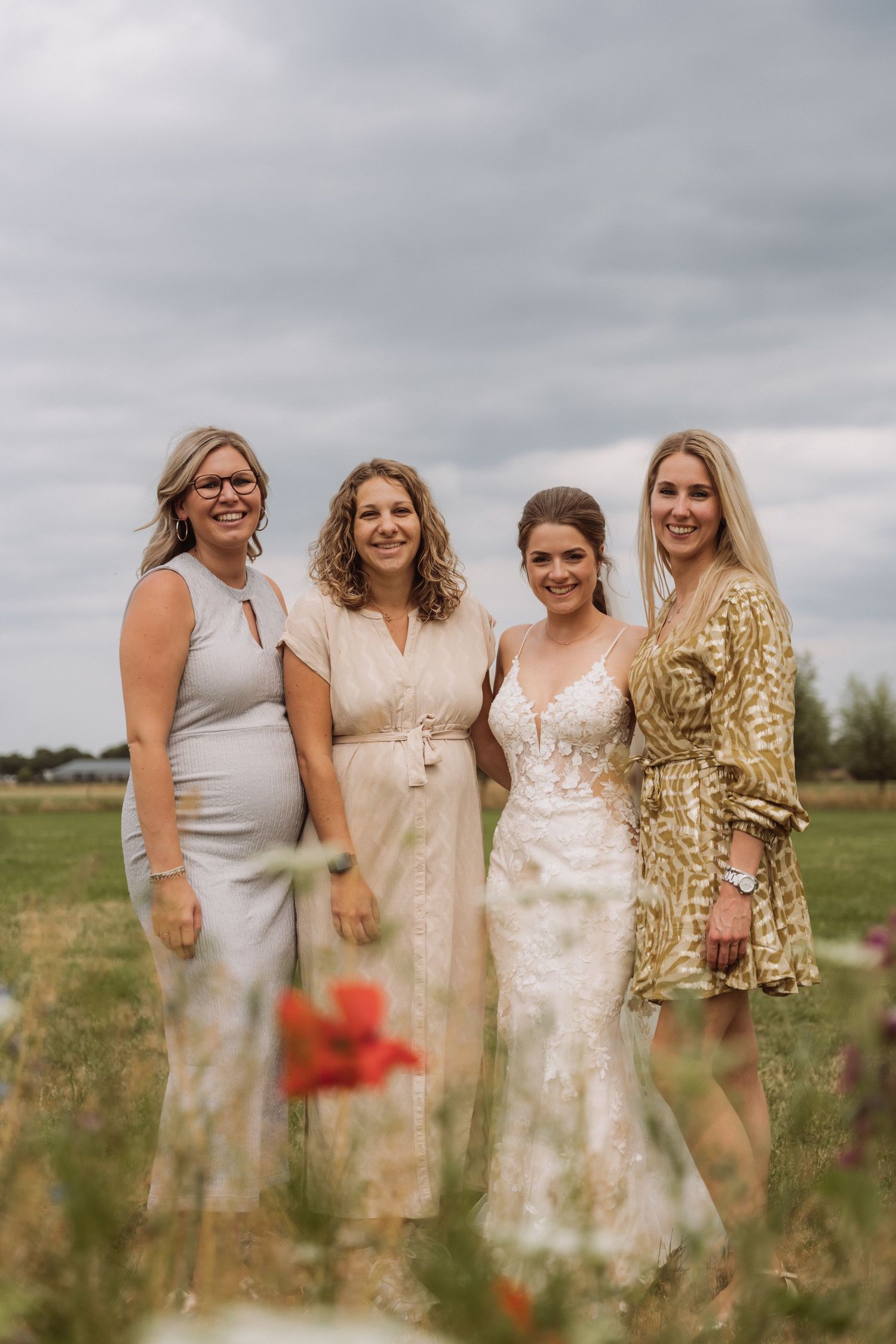 Group of wedding guests in neutral and gold dresses pose together in a summer field.