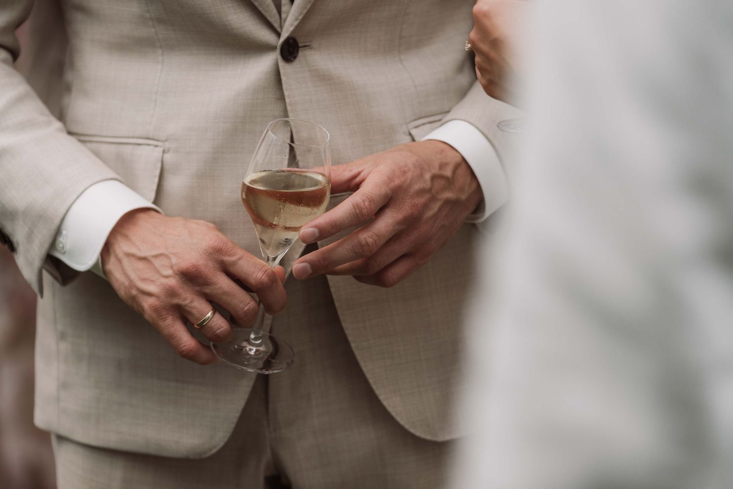Close-up detail of hands holding champagne glasses in formal attire at an elegant event.