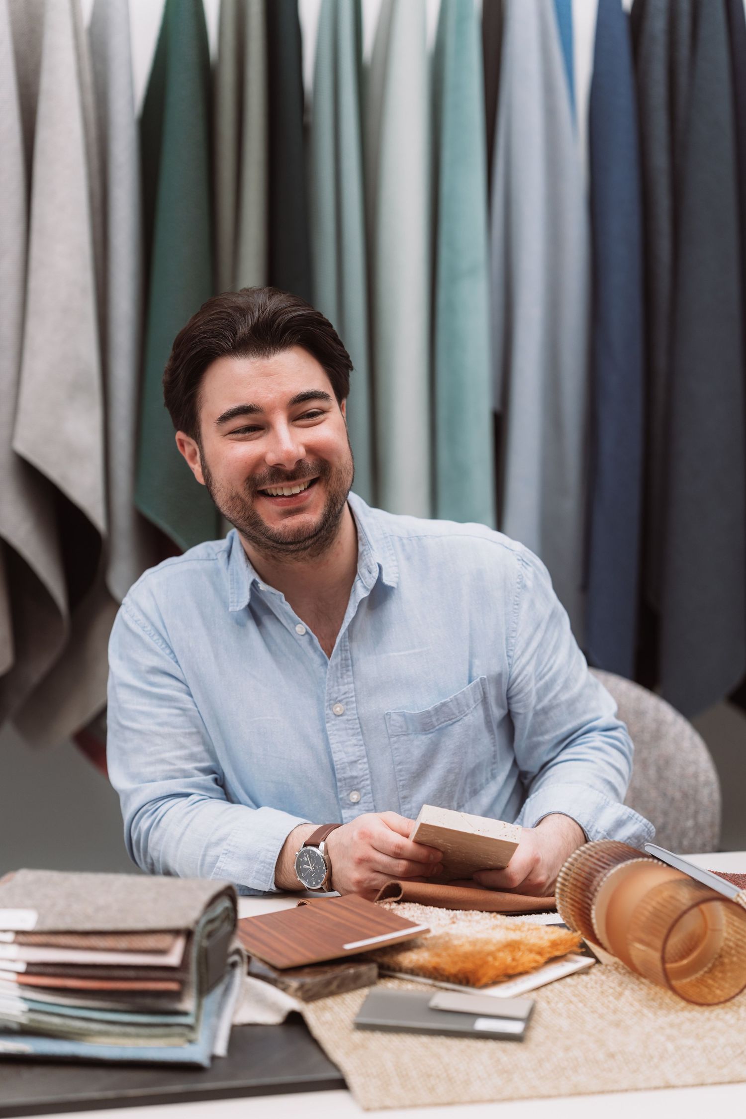 Person in light blue shirt smiling while sitting at desk with books and papers spread out.