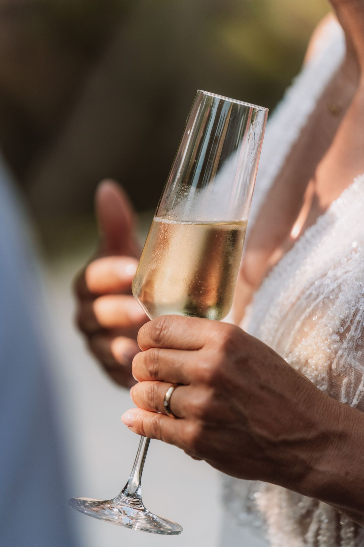 Close-up shot of hands holding champagne glasses with a wedding ring visible during a celebration.