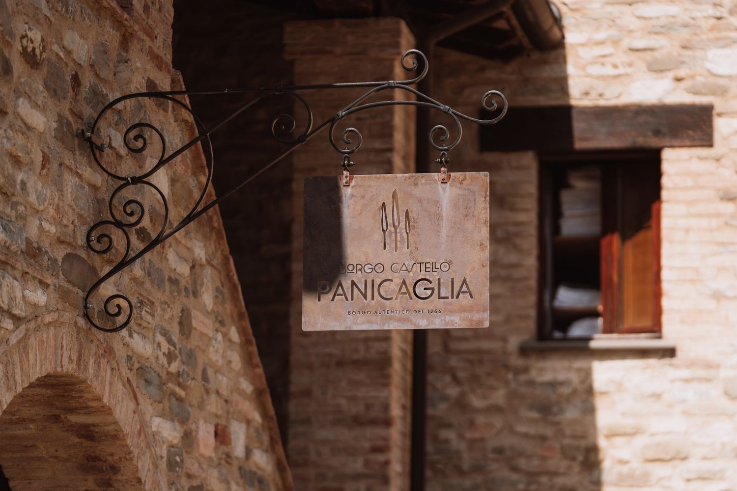 Rustic stone wall with decorative wrought iron details and vintage signage in an Italian village.