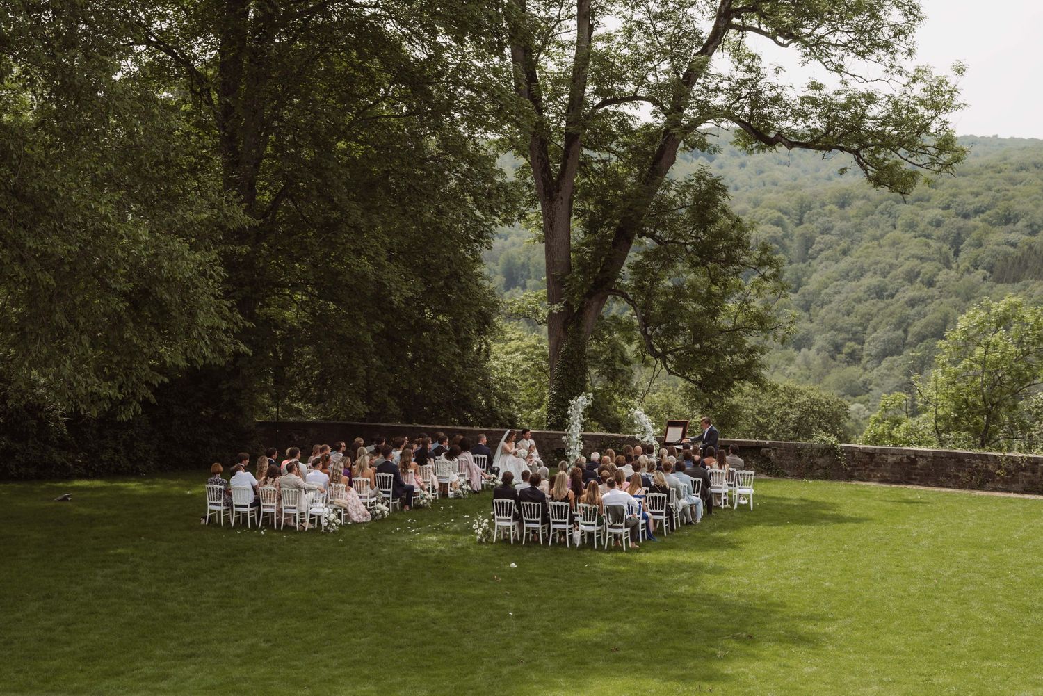A scenic outdoor wedding ceremony setup with white chairs arranged on a lush green hillside overlooking mountain views.