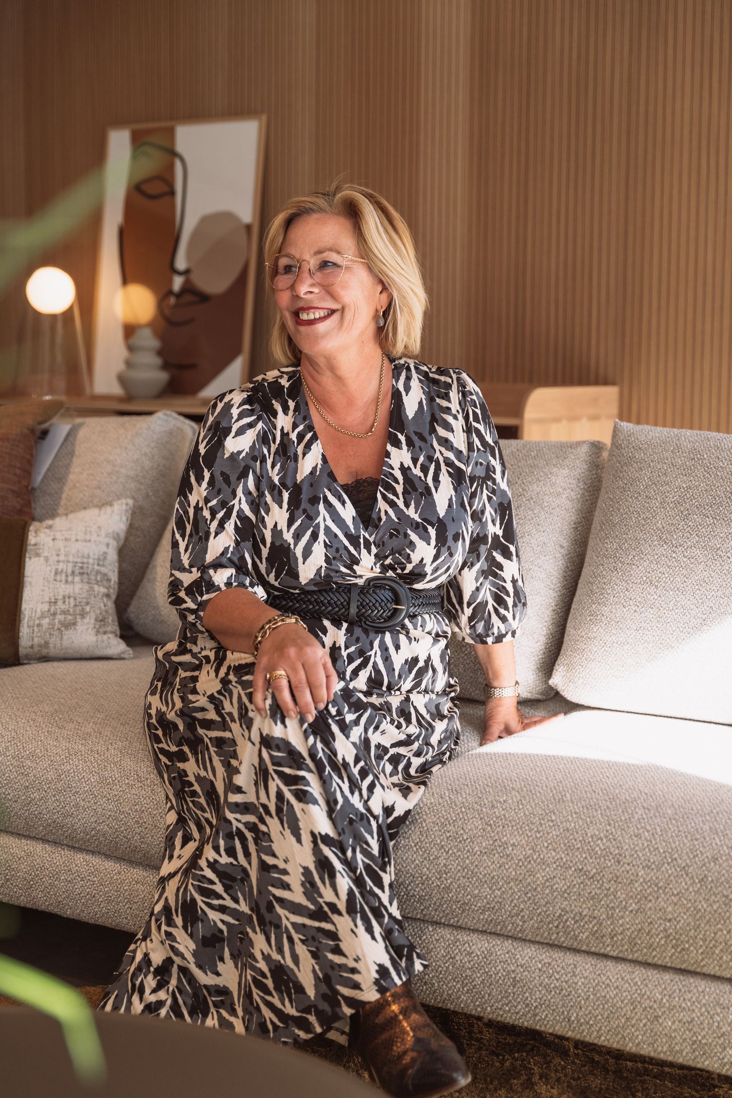 A person in a black and white patterned dress sits comfortably on a light gray couch while laughing and relaxing.