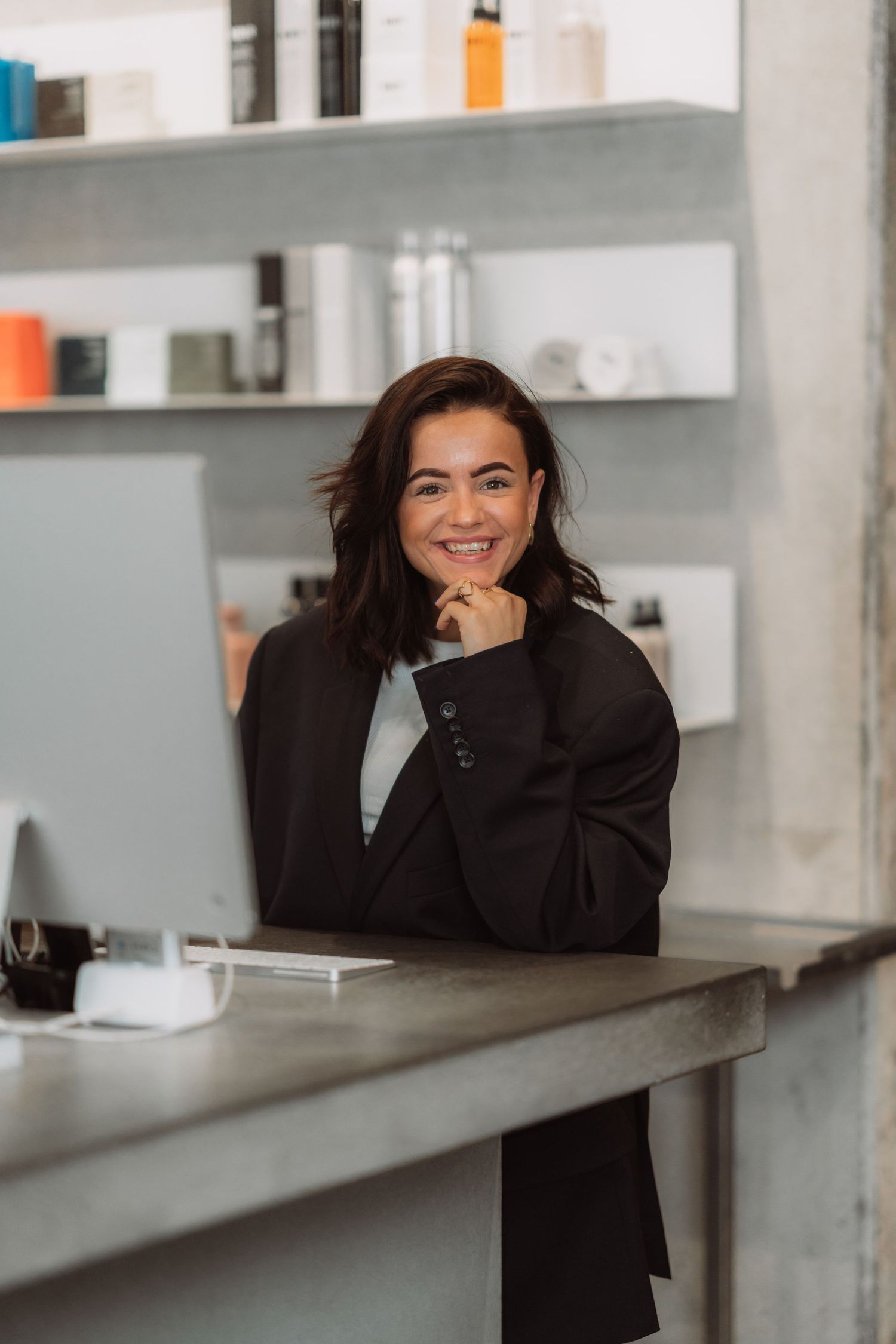 Person in black jacket leaning on white counter in modern salon setting.