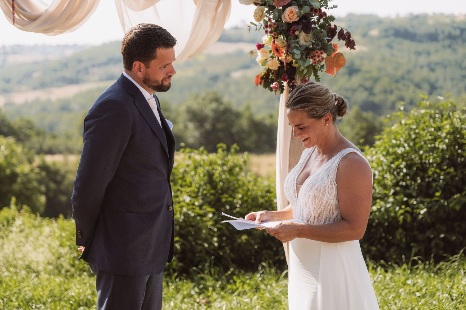 A couple exchanges vows during an outdoor wedding ceremony with scenic mountain views in the background.