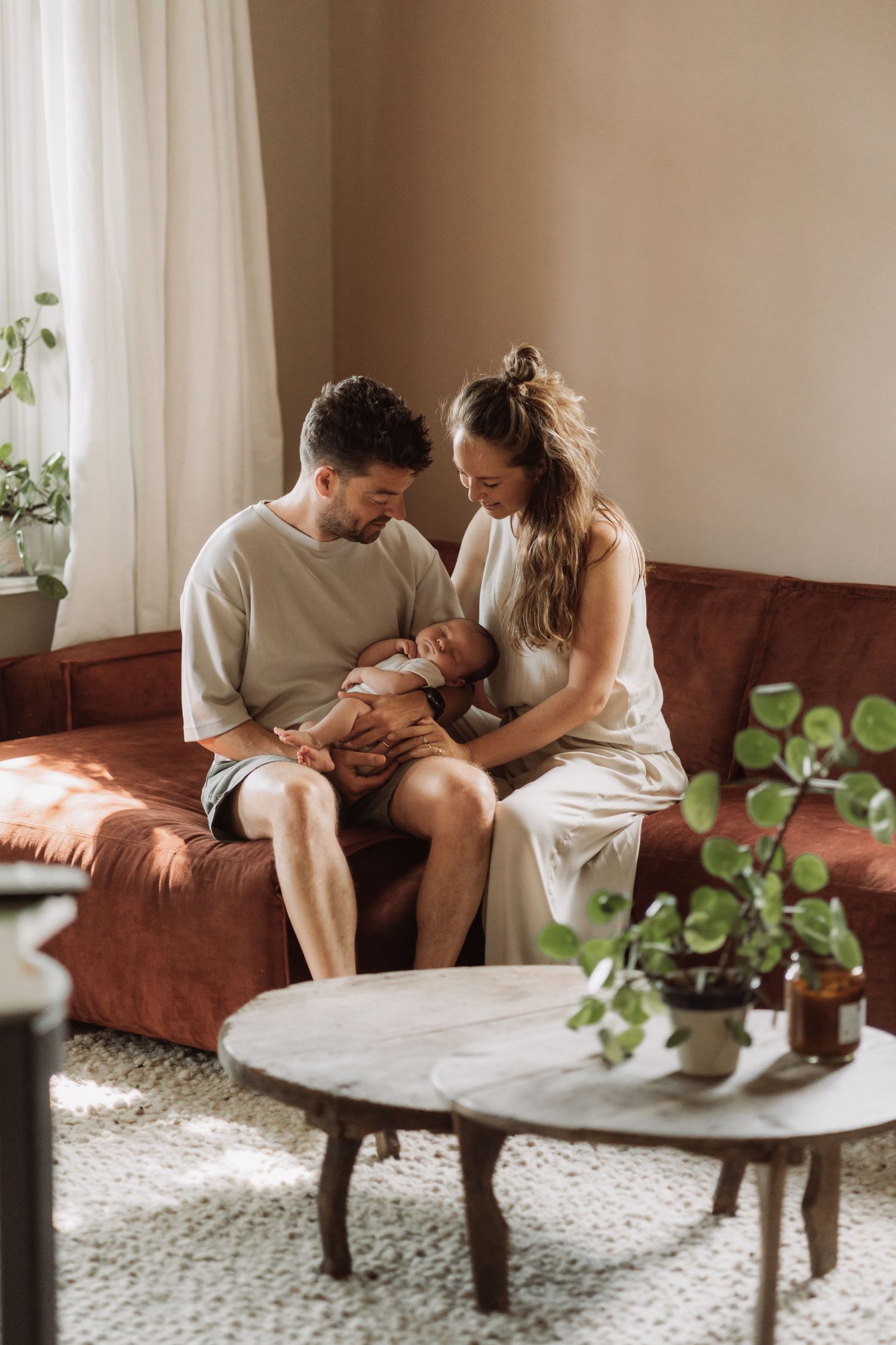 Intimate couple lounging together on brown couch in bright, plant-decorated living room.