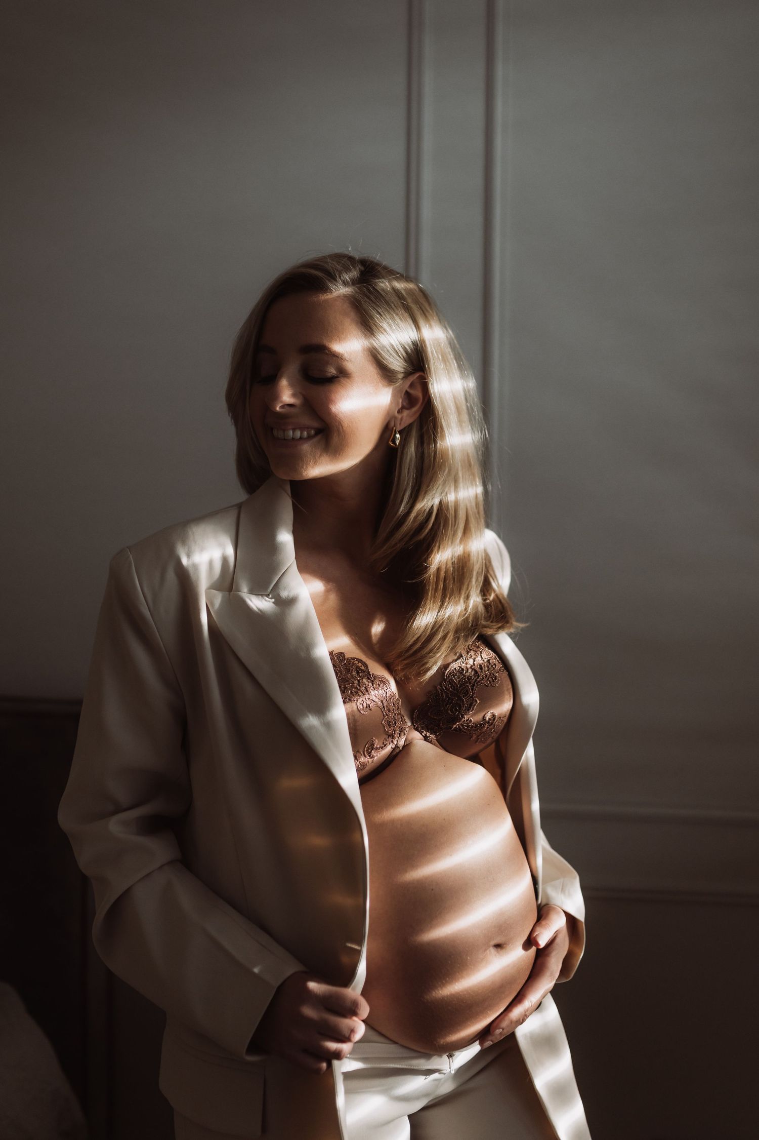 Artistic maternity photoshoot featuring dramatic lighting and shadows in an indoor setting.
