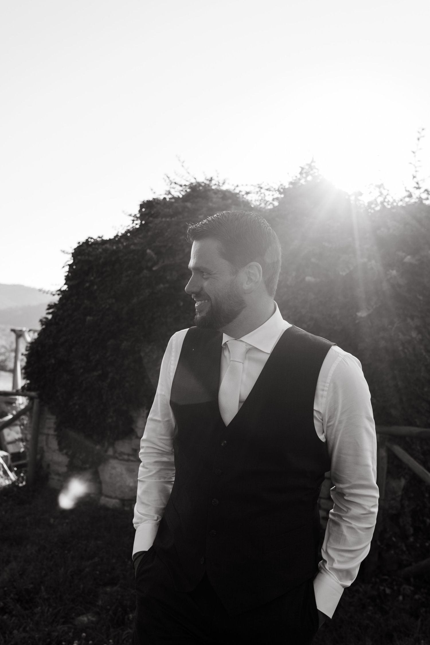 A series of black and white photos showing people in formal attire standing outdoors with sunlight filtering through trees.