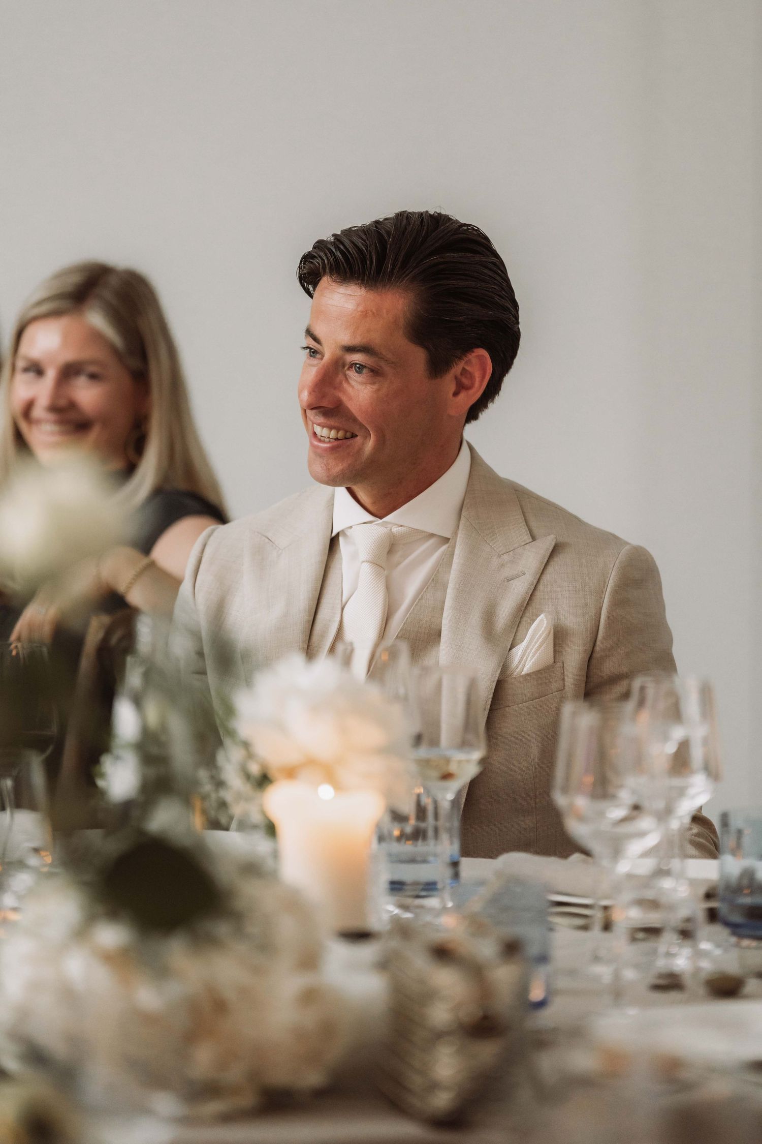 Elegant wedding reception table setting with glowing candles and guests seated in a bright, airy dining room.