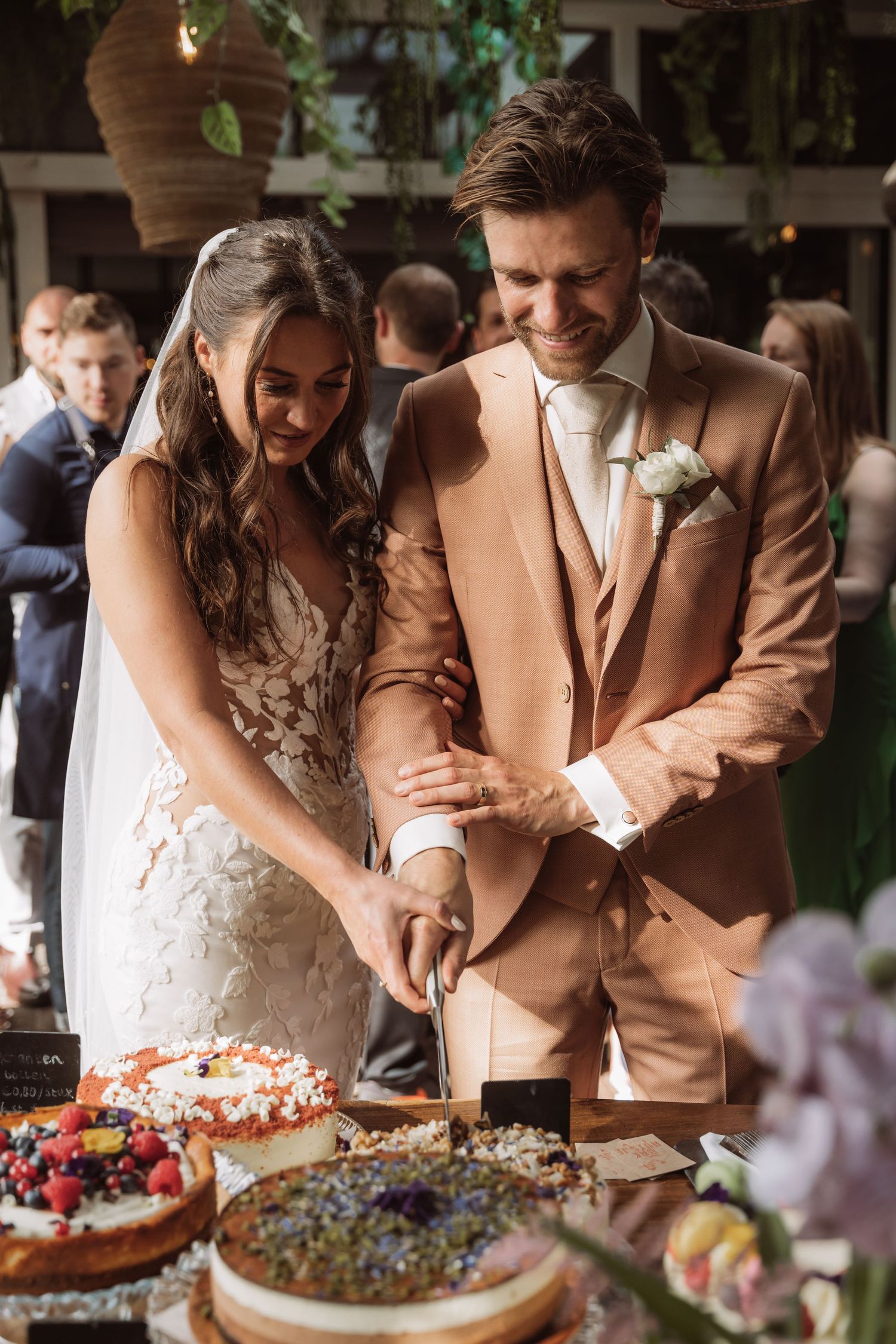 A couple in wedding attire cut into colorful desserts together at their reception celebration.