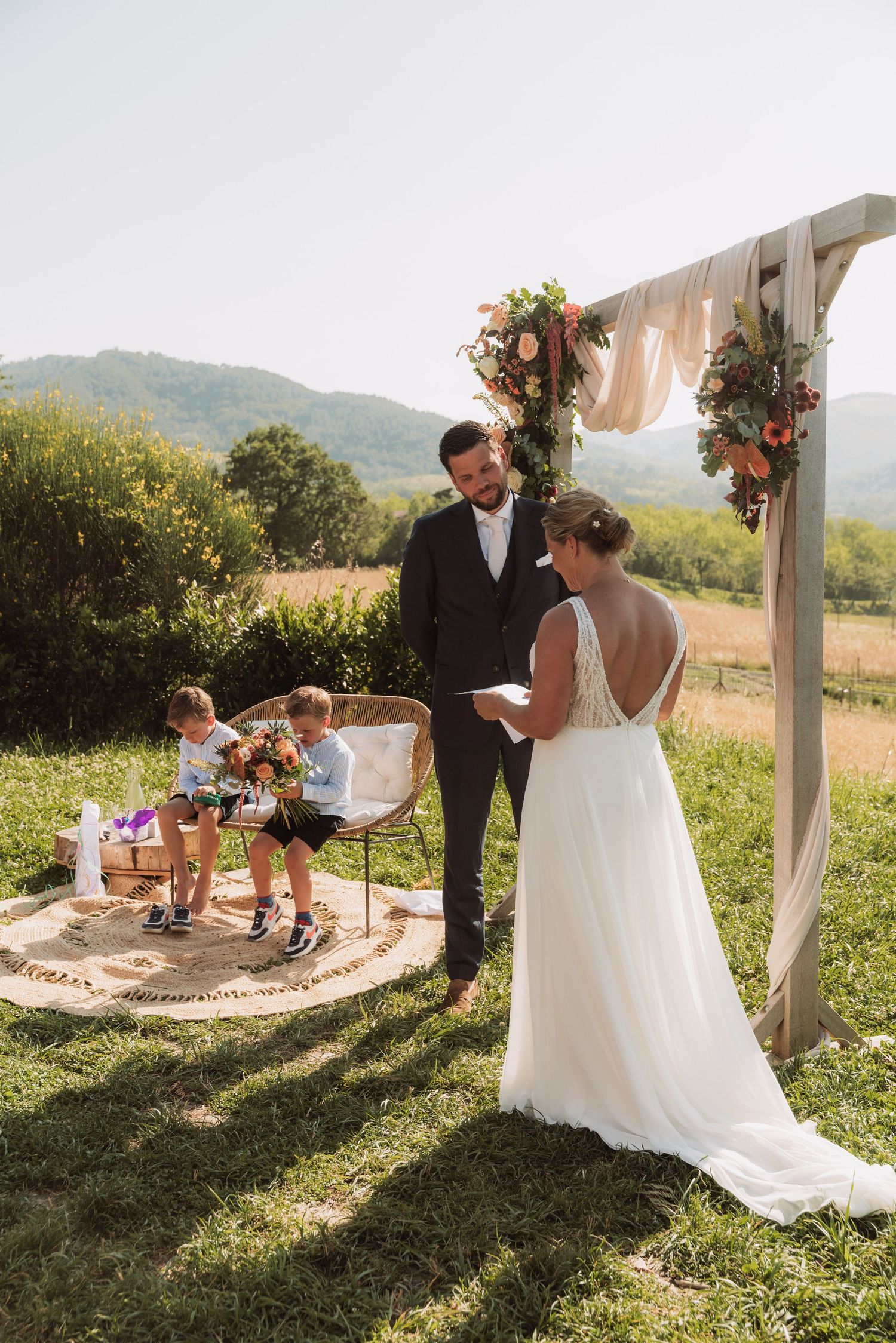 Romantic outdoor wedding ceremony in a scenic mountain setting with floral arch and rustic seating arrangements.