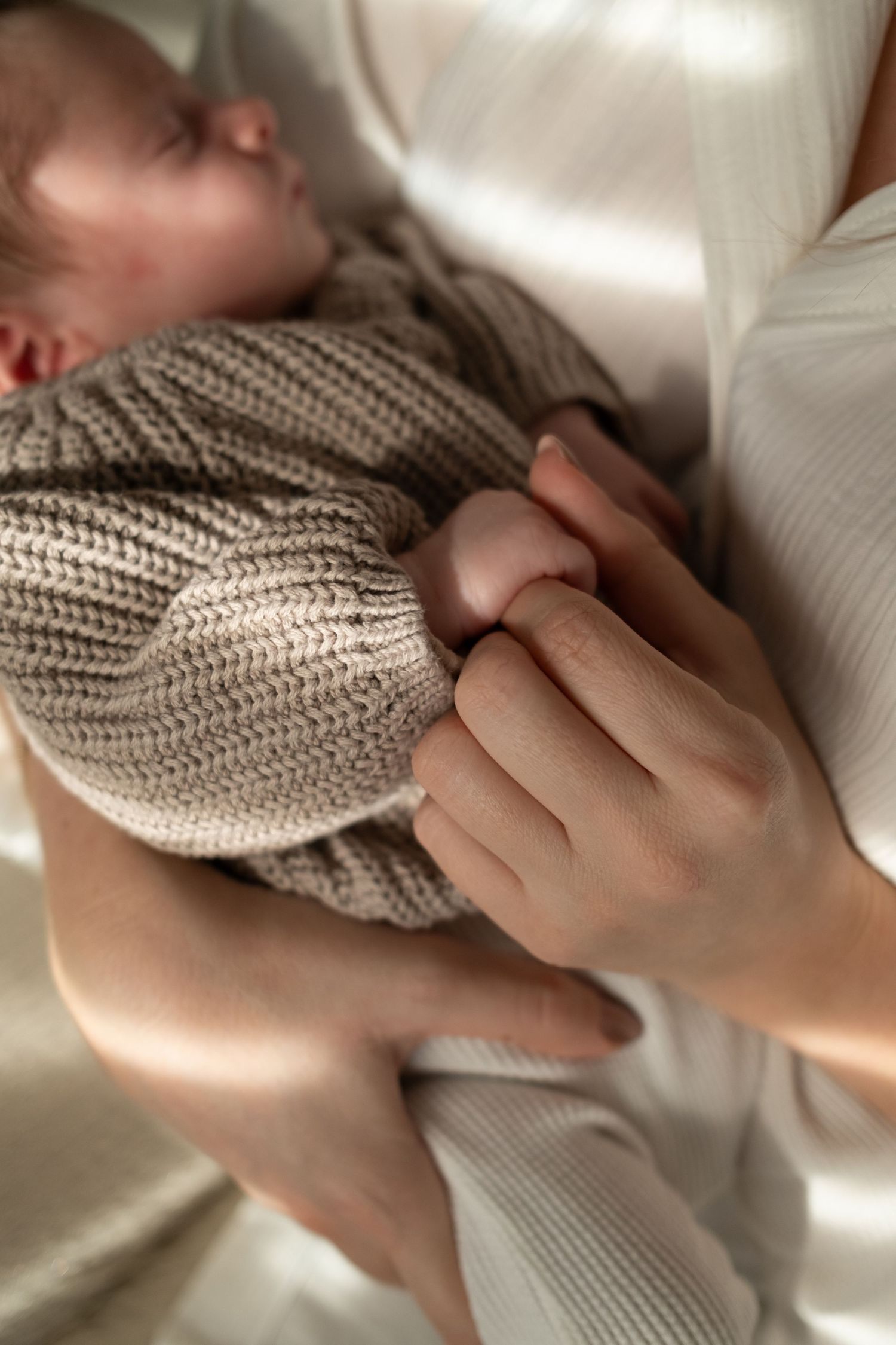 Close-up of gentle hands holding a sleeping infant in knit clothing.