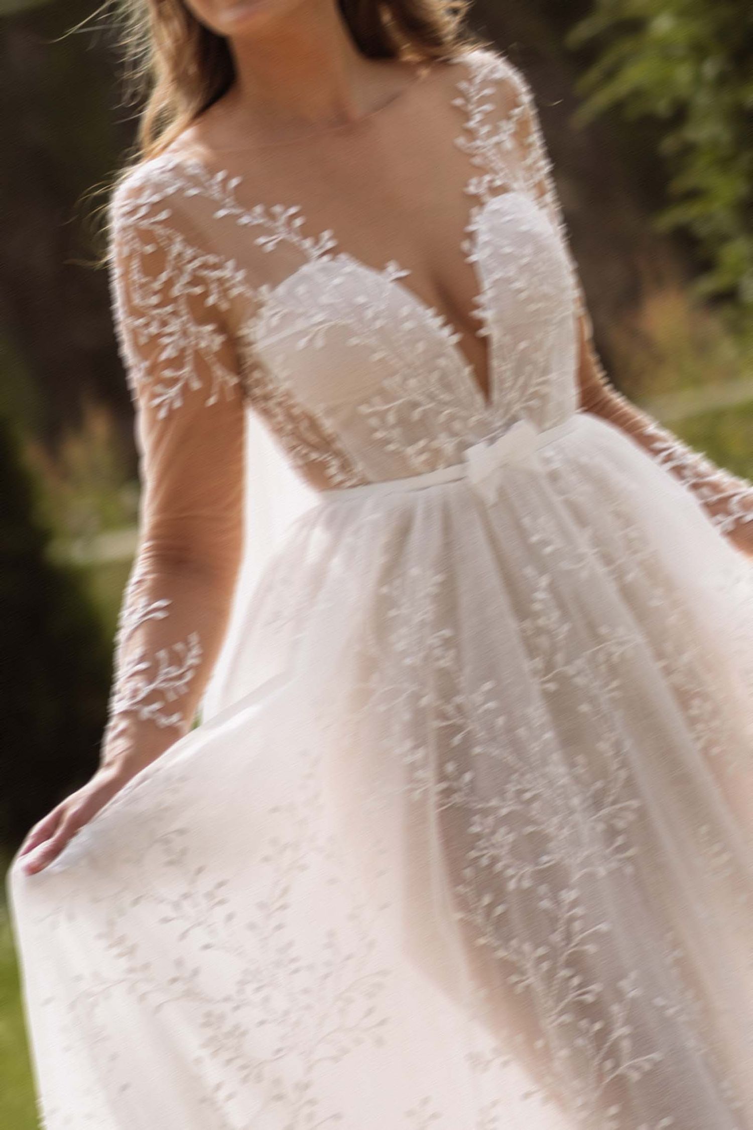 Close-up details of a white lace wedding dress with delicate embroidery and flowing tulle fabric in an outdoor setting.