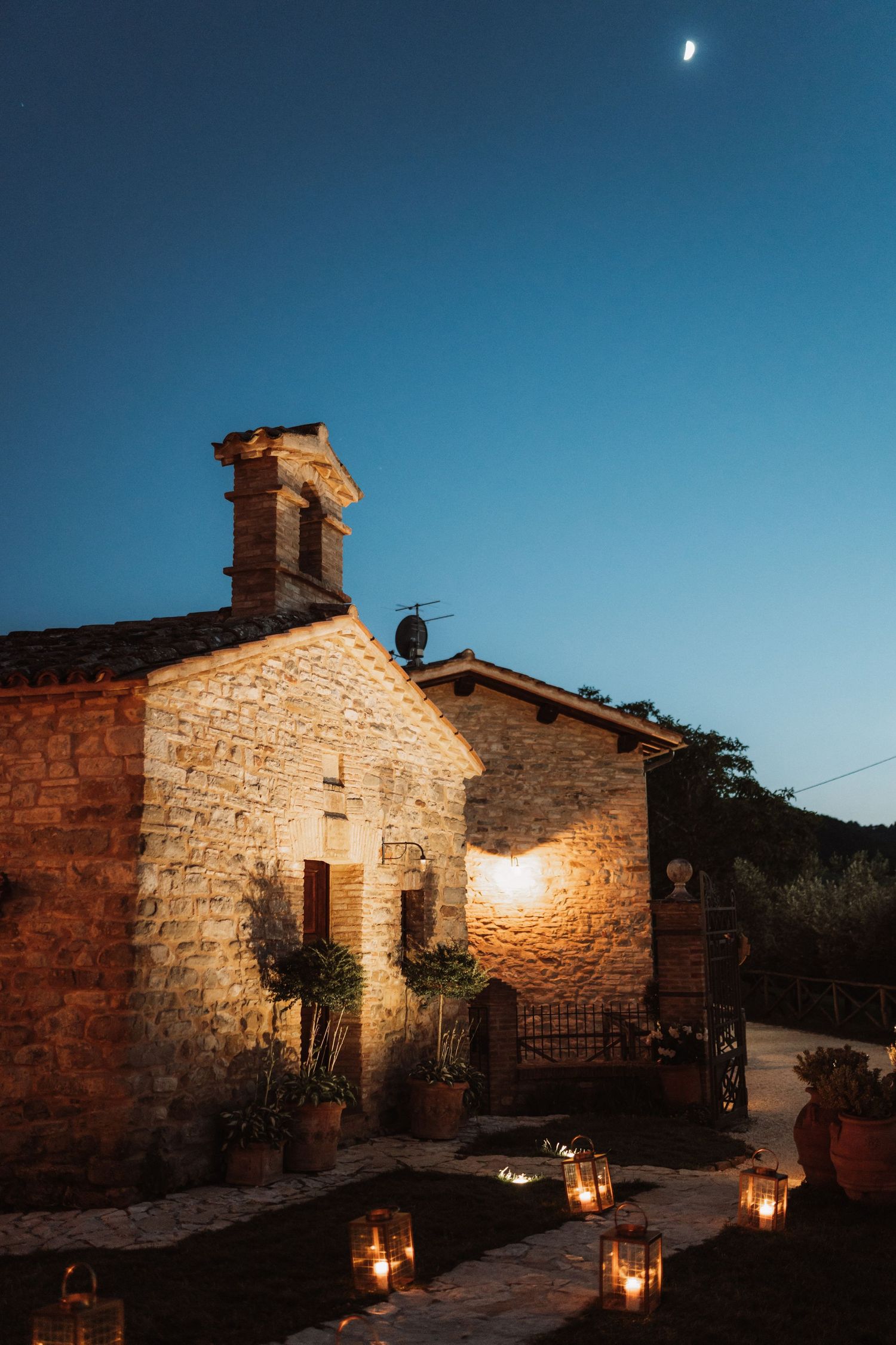 Stone buildings illuminated by lanterns and moonlight create a romantic rustic atmosphere at dusk.