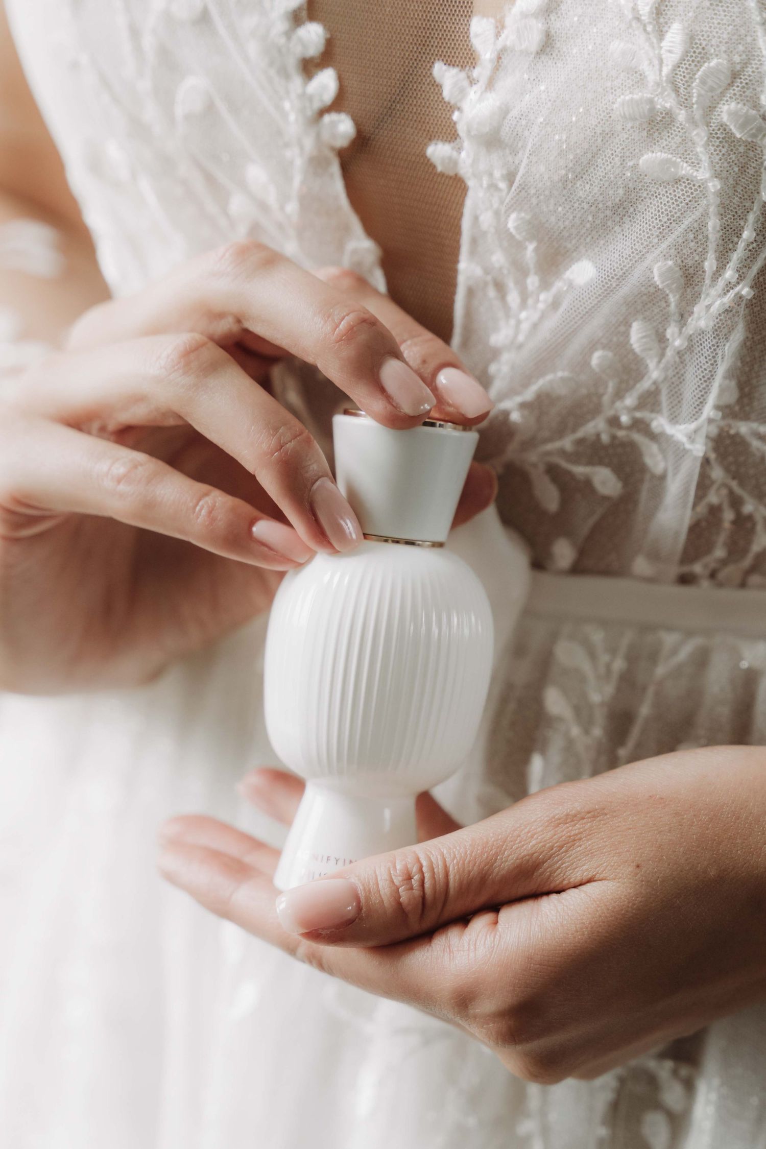 Hands gently hold a small white ribbed ceramic vase against a delicate lace background.