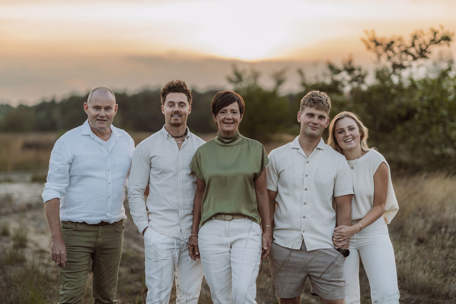 Group of five people in coordinated casual outfits posing at sunset.