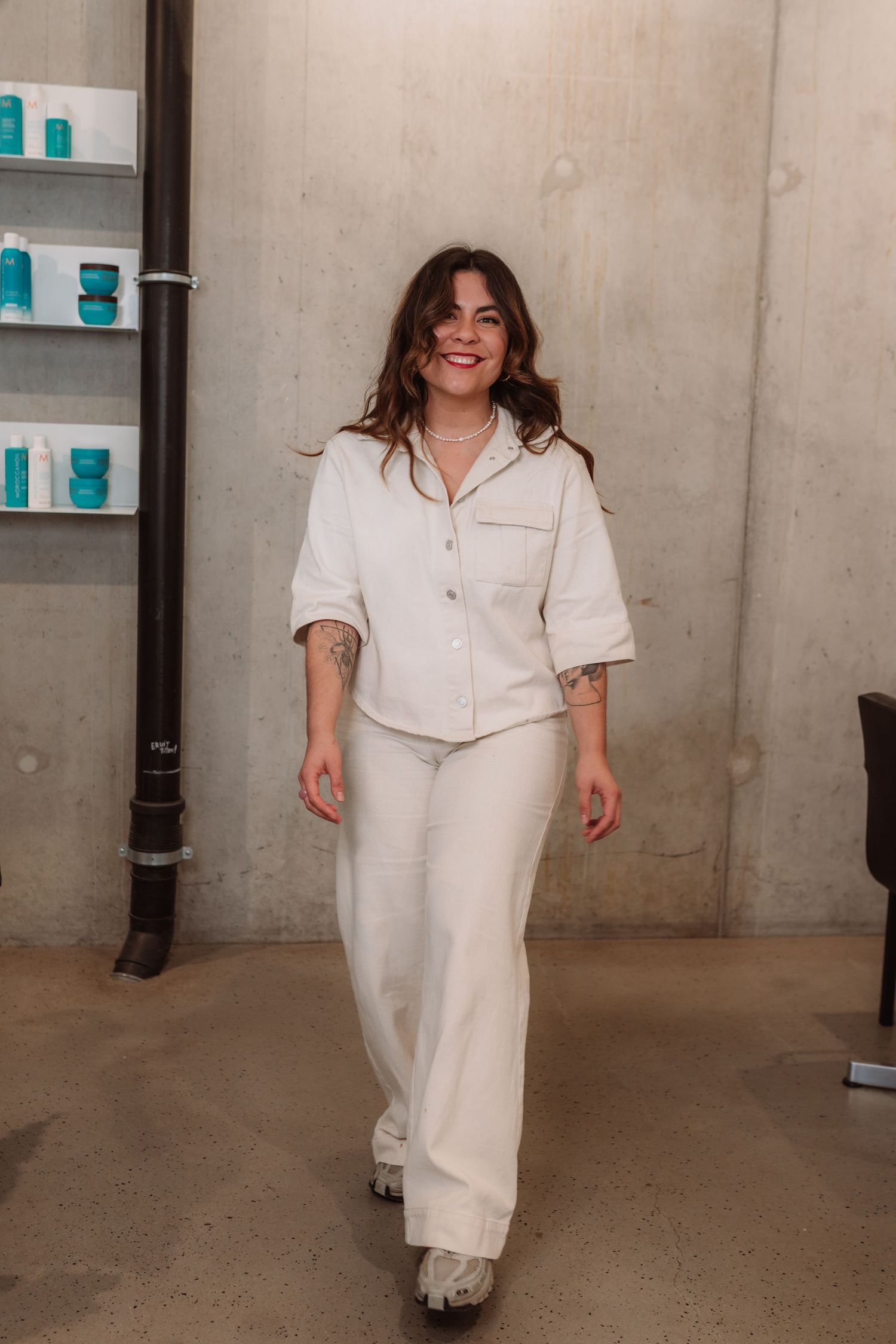 Stylist in all-white uniform walking confidently through a modern salon space.