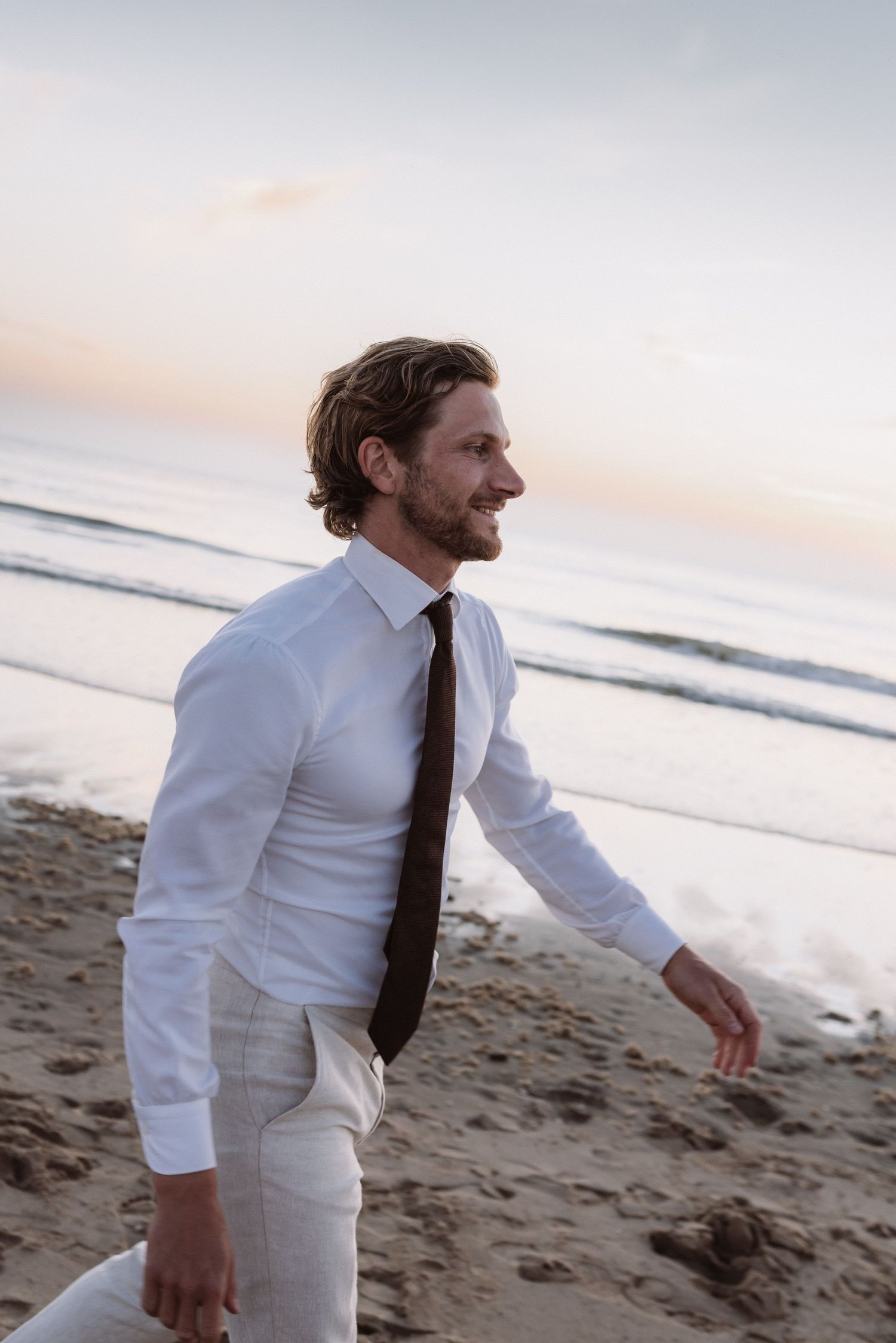 Man in white shirt and tie enjoying a moment on the beach at sunset.