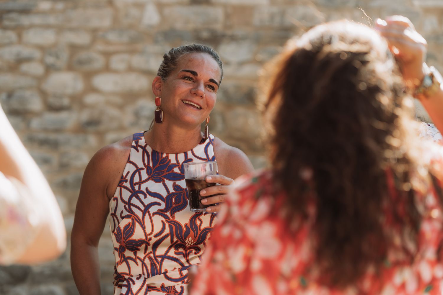 People enjoying conversation and laughter at an outdoor gathering with stone walls in the background.