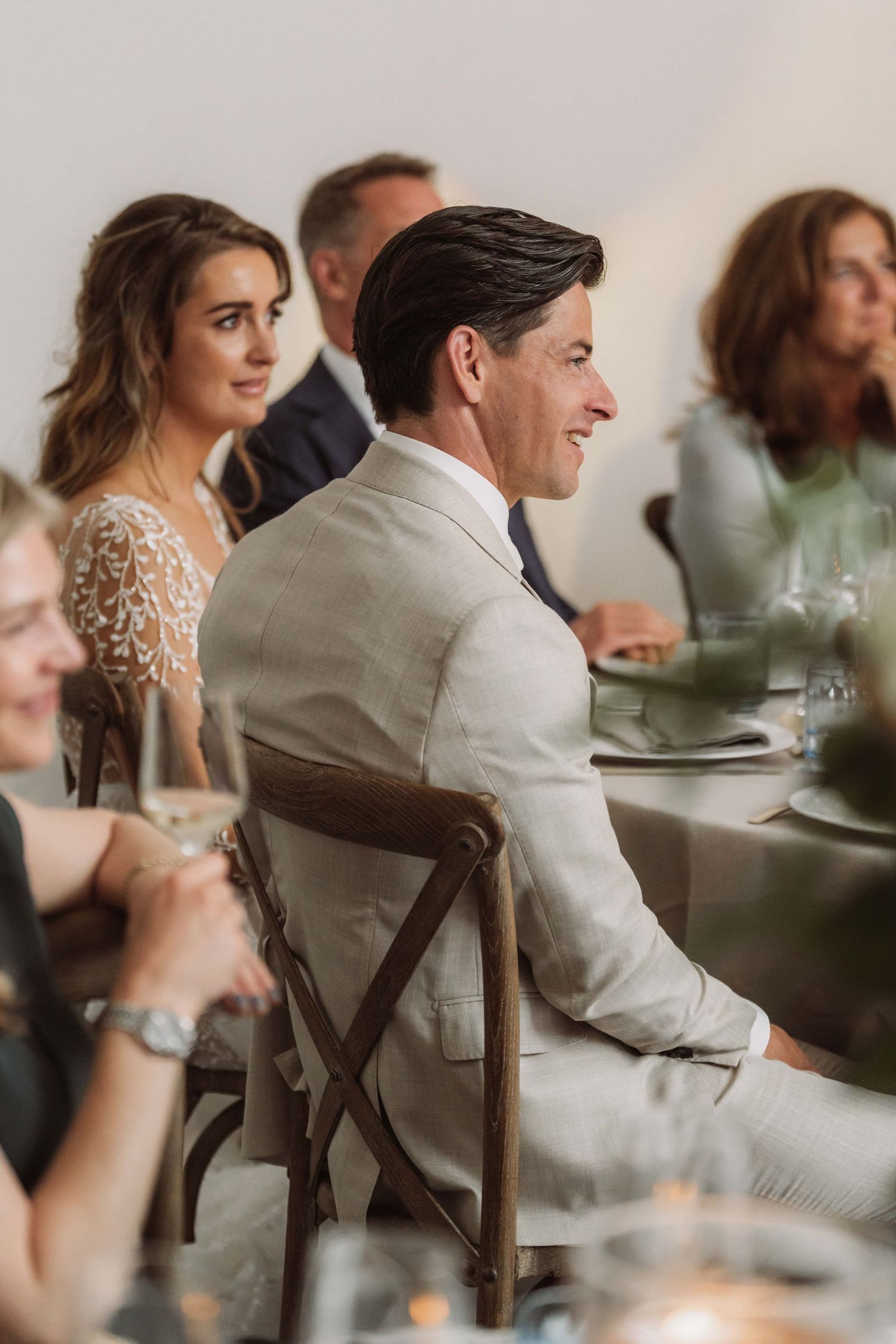 Guests seated at wedding reception tables engage in lively conversation in an elegant indoor setting.