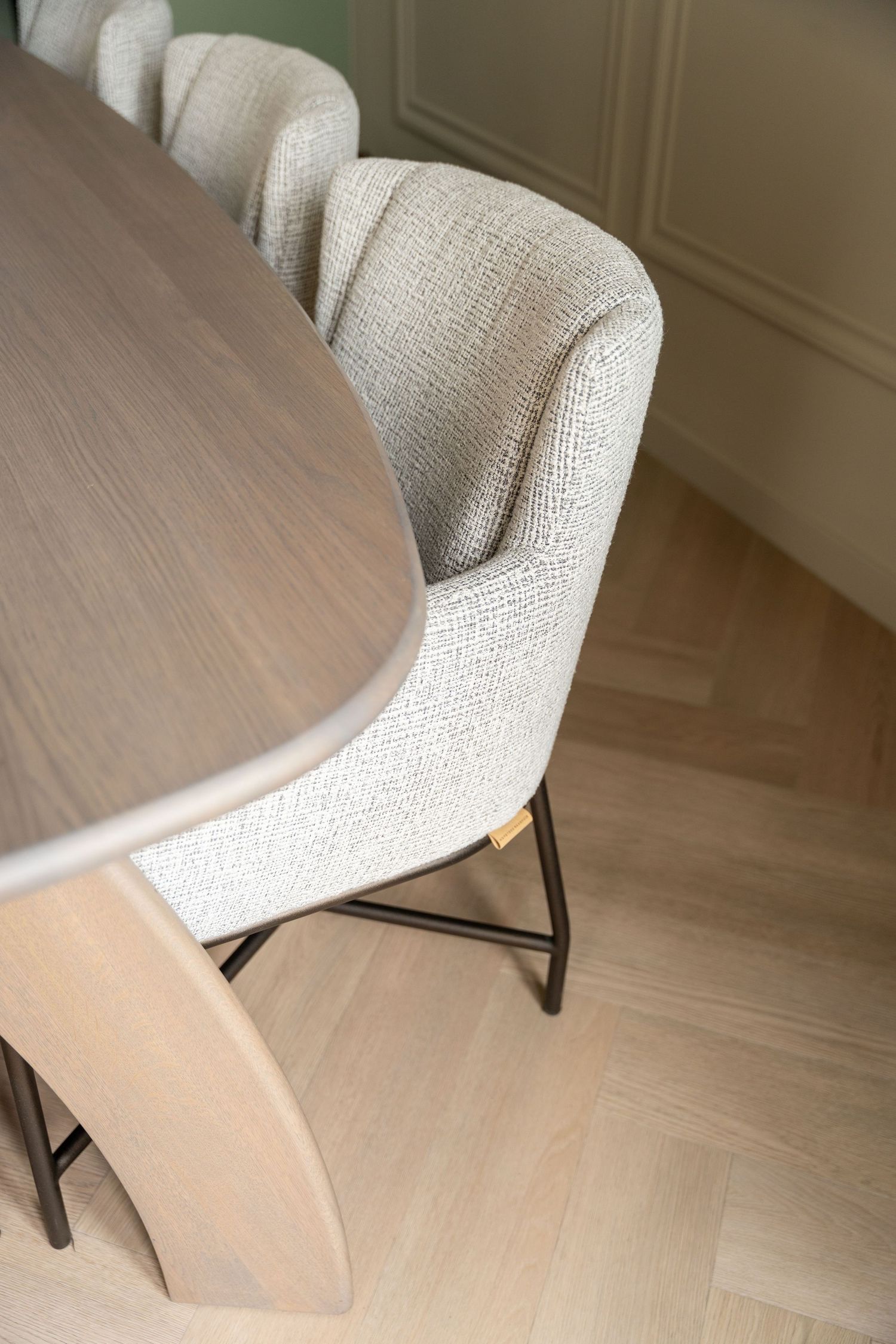 Modern dining room chairs with cream textured upholstery and metal legs alongside a wooden oval table on light flooring.